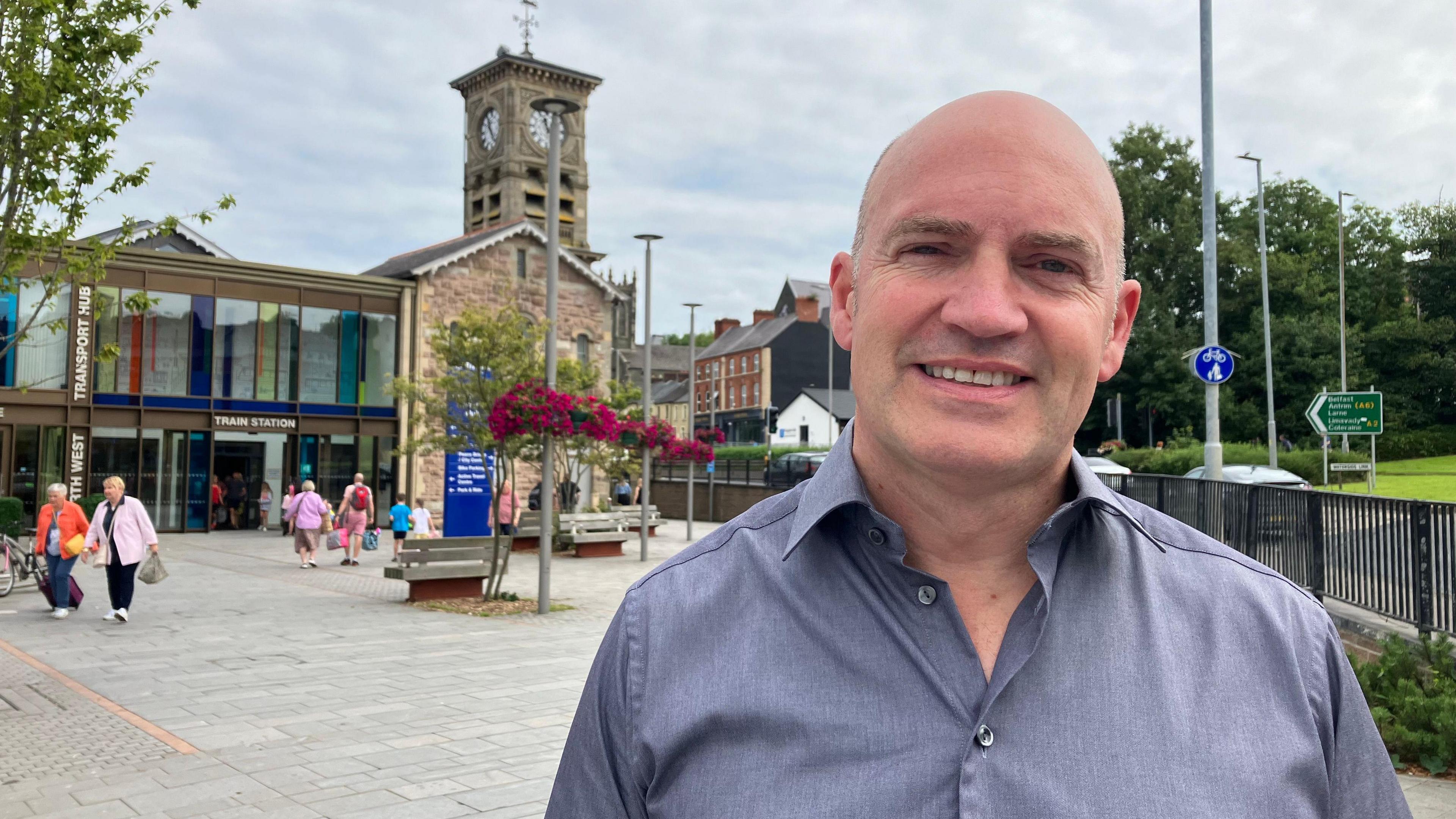 Man standing looking at the camera with a train station behind him