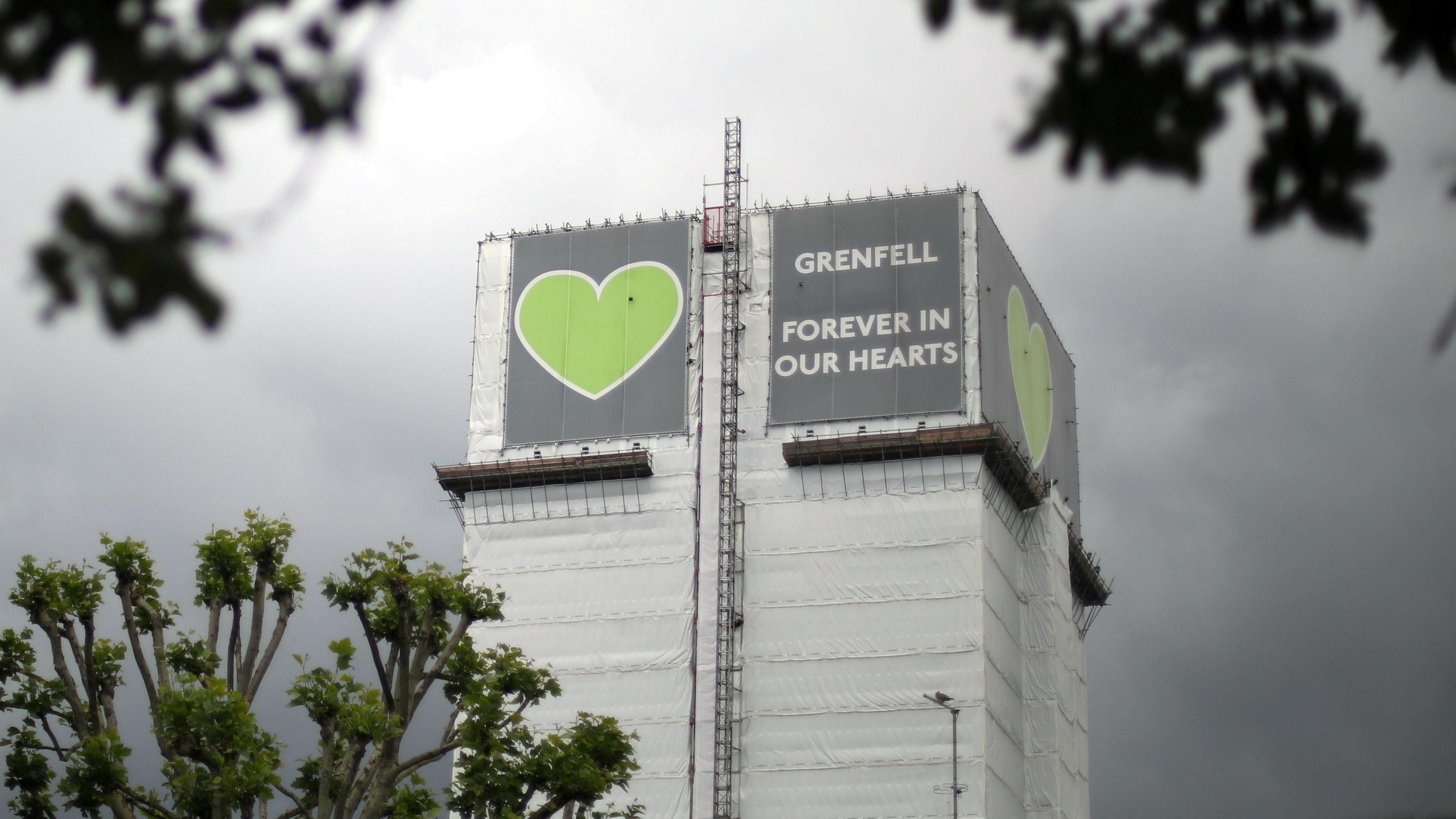 File image of Grenfell Tower covered by tarpaulin and scaffolding, with the grey and green 'Grenfell - forever in our hearts' sign at the top 