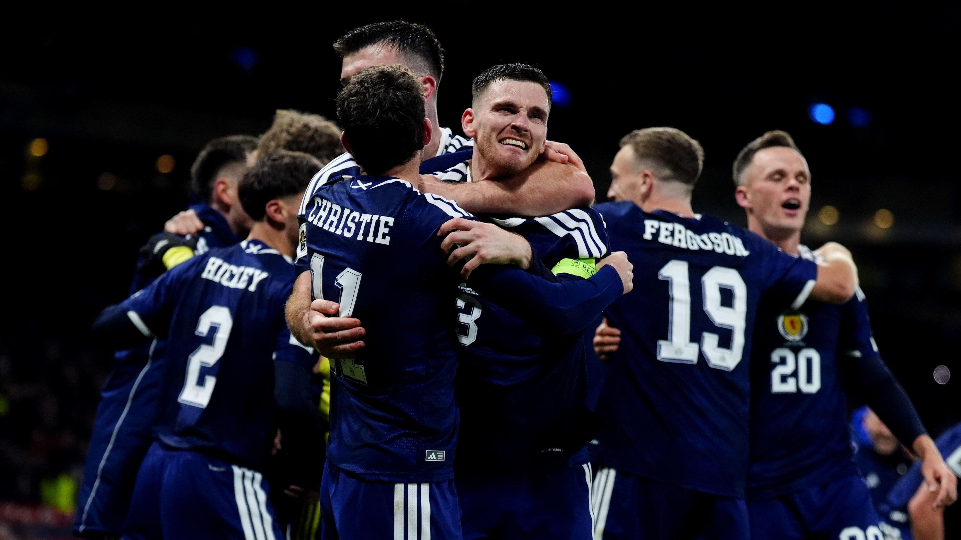 Players for the Scotland's men's football team hug in their navy football strips on the pitch during the match with Denmark. Andy Robertson can be seen looking emotional.