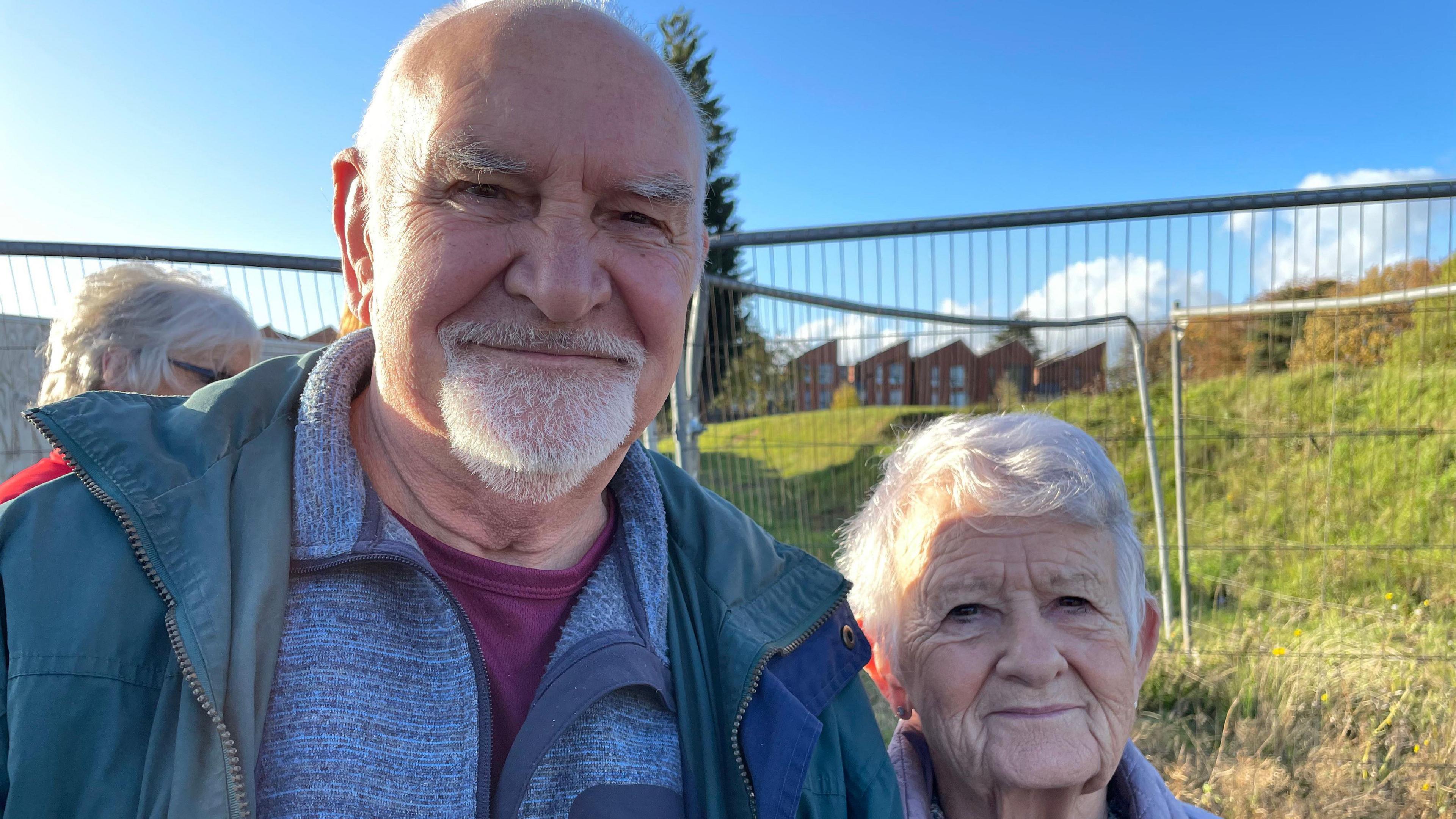 Bald man with a beard and green jacket alongside woman with grey hair