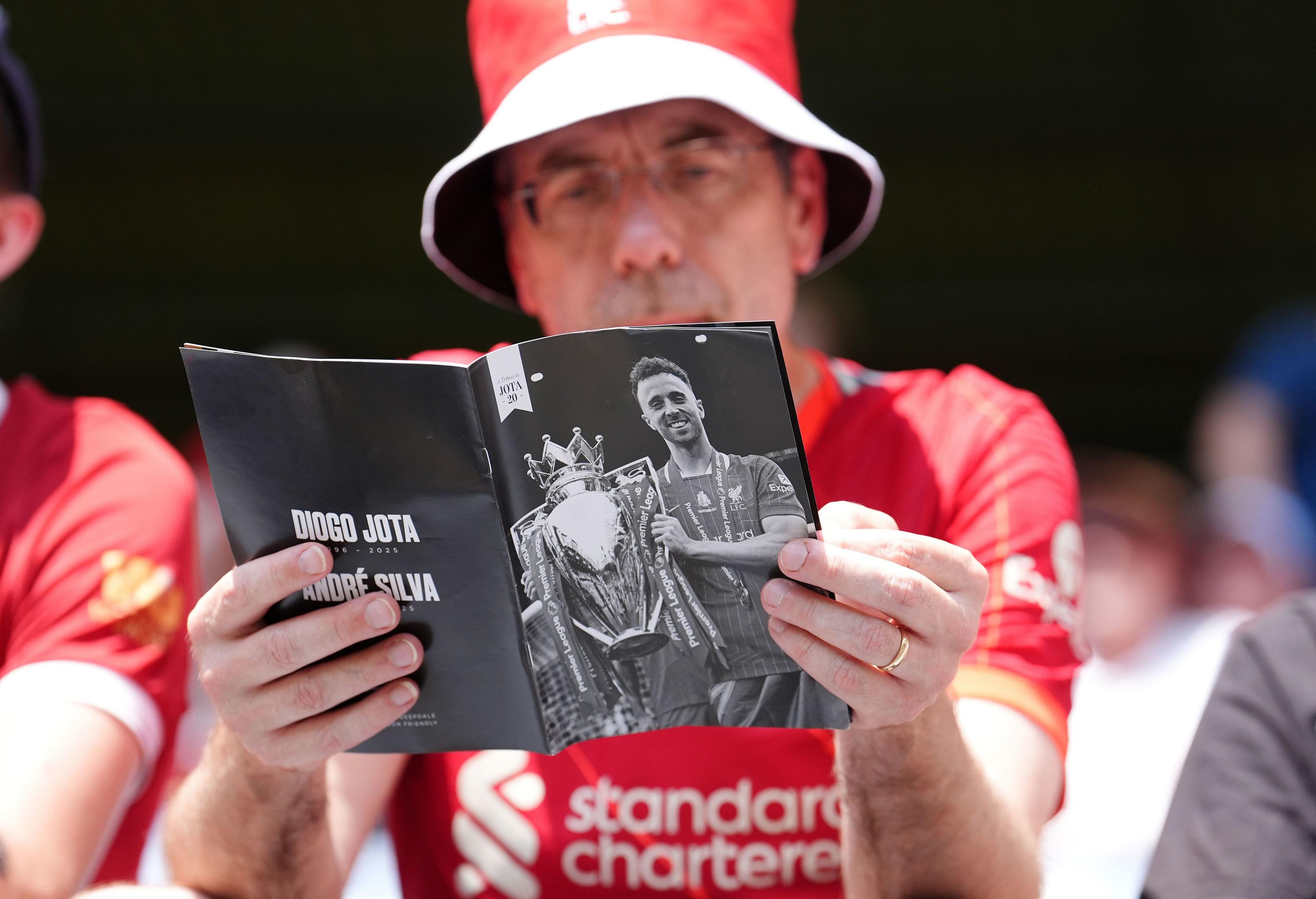 Liverpool fan reads programme with picture of Diogo Jota on the cover
