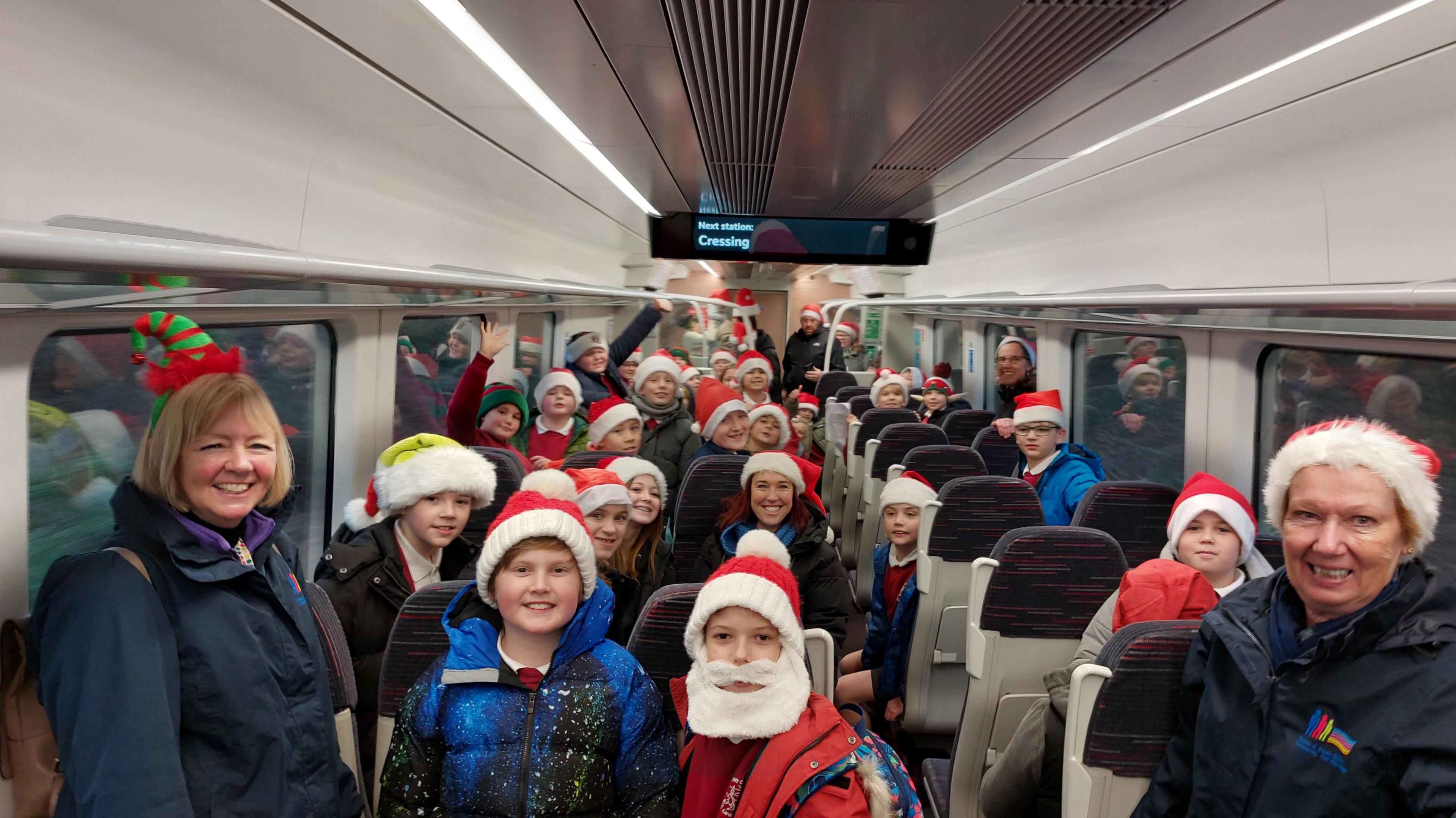 Children are crammed onto the train carriage. They are wearing Santa hats, scarfs and coats. One boy is wearing a false white beard. They are all looking at the camera