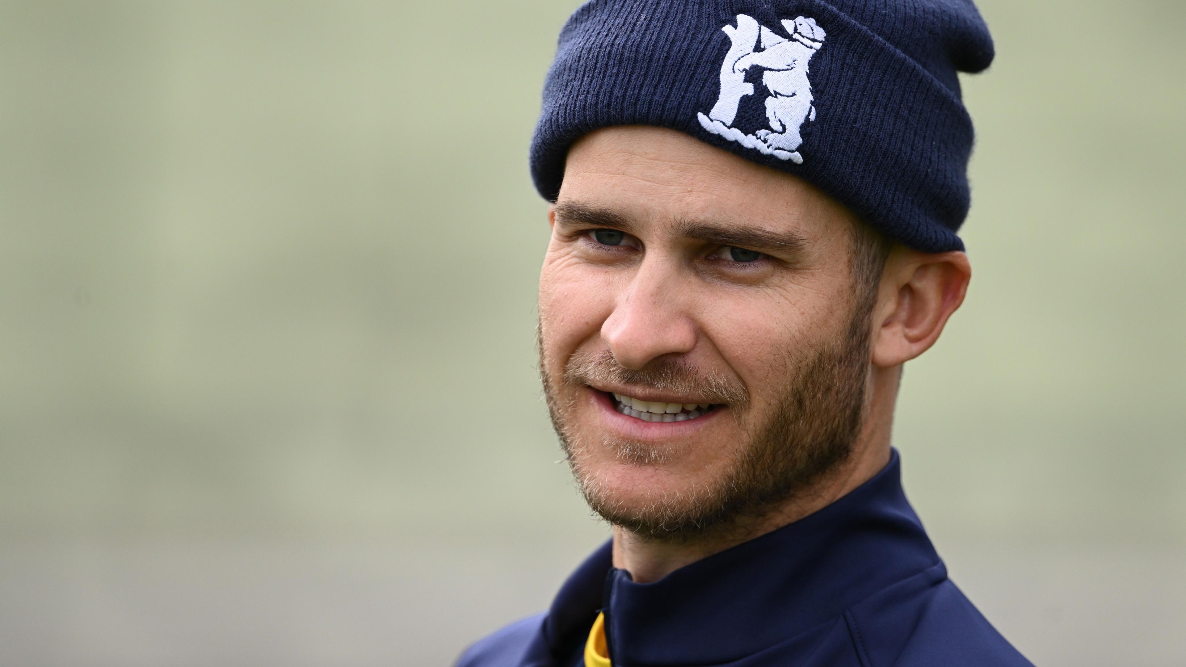 Sam Hain looks on wearing a blue hat with a Warwickshire cricket crest on the front