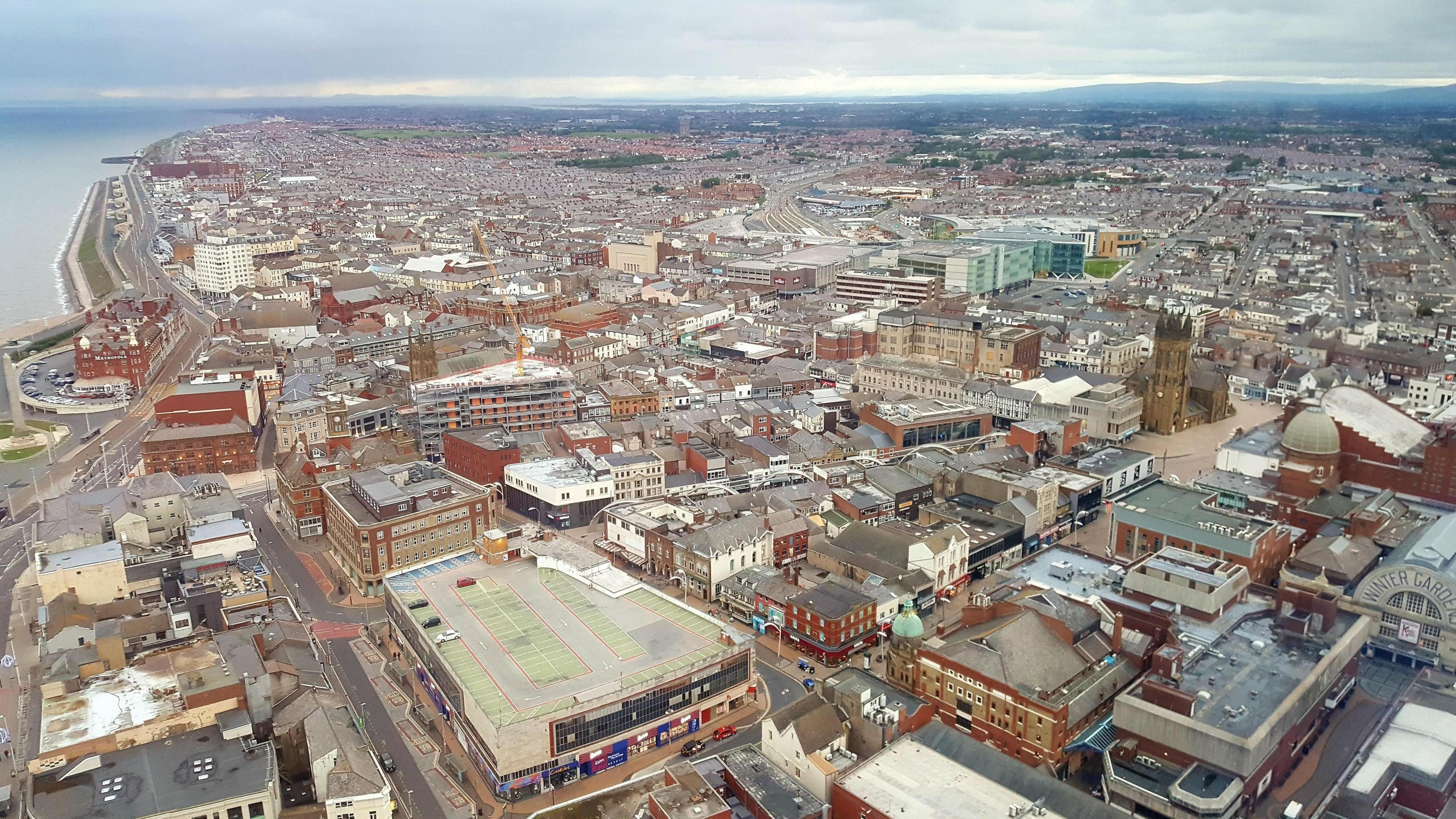 Aerial view of Blackpool town centre showing the sea and Promenade on the right hand side of the image. Most buildings are just two or three storeys high, many with flat roofs. The Winter Gardens building is in the bottom right corner.