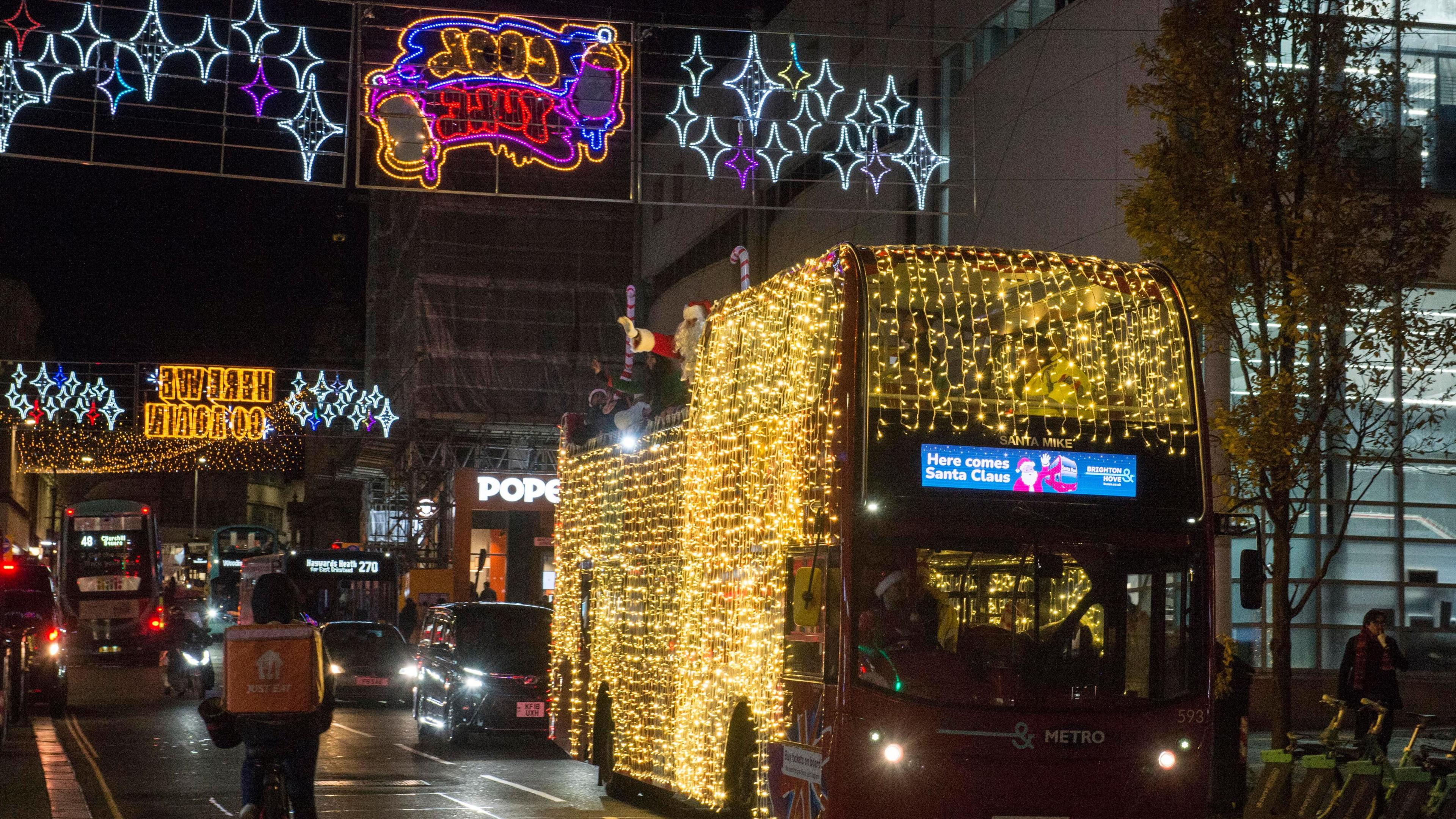 A double decker bus covered in Christmas lights being driven through busy streets in Hove.