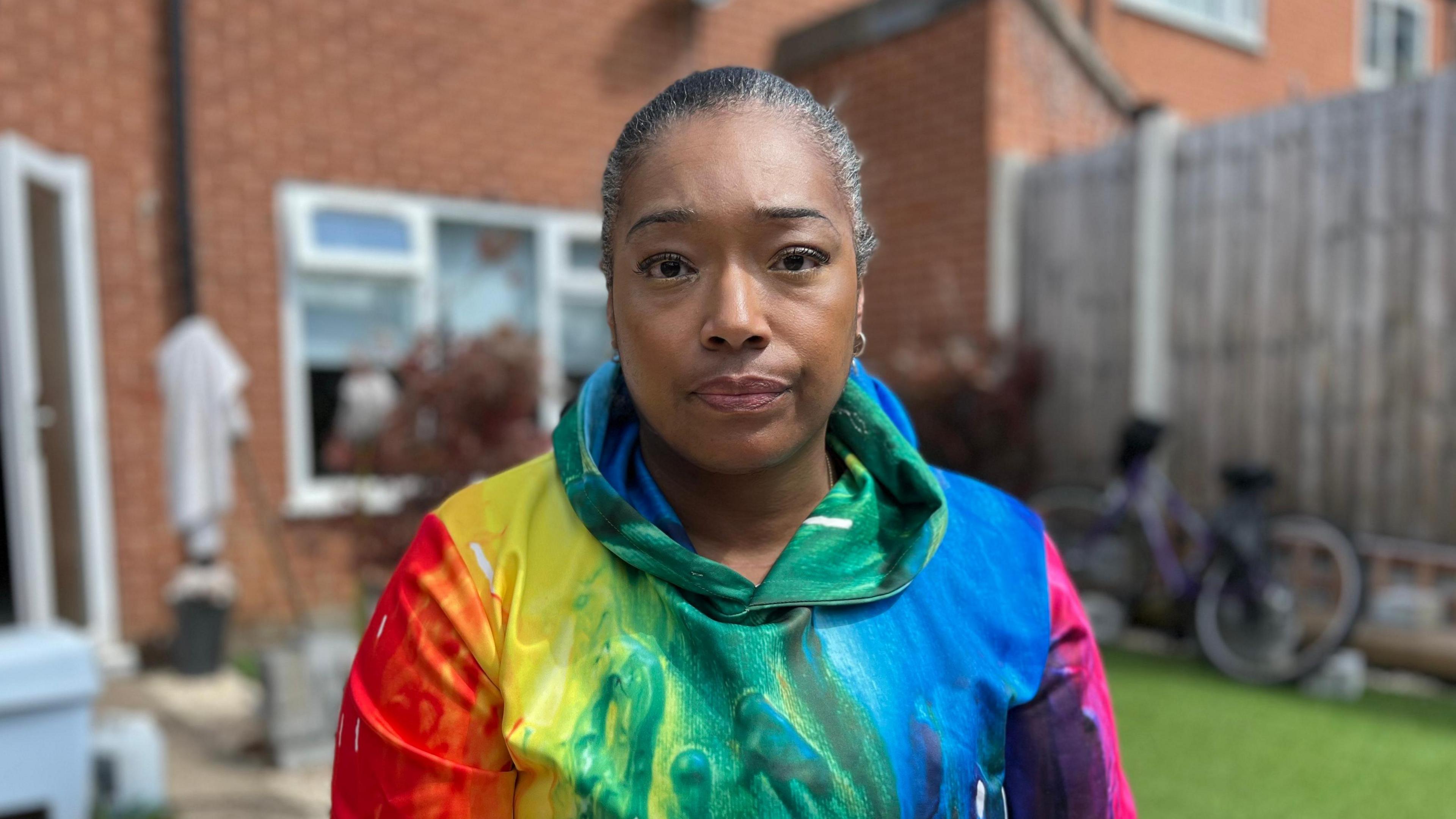 Deborah Williams in her garden wearing a bright, multi-coloured hoodie