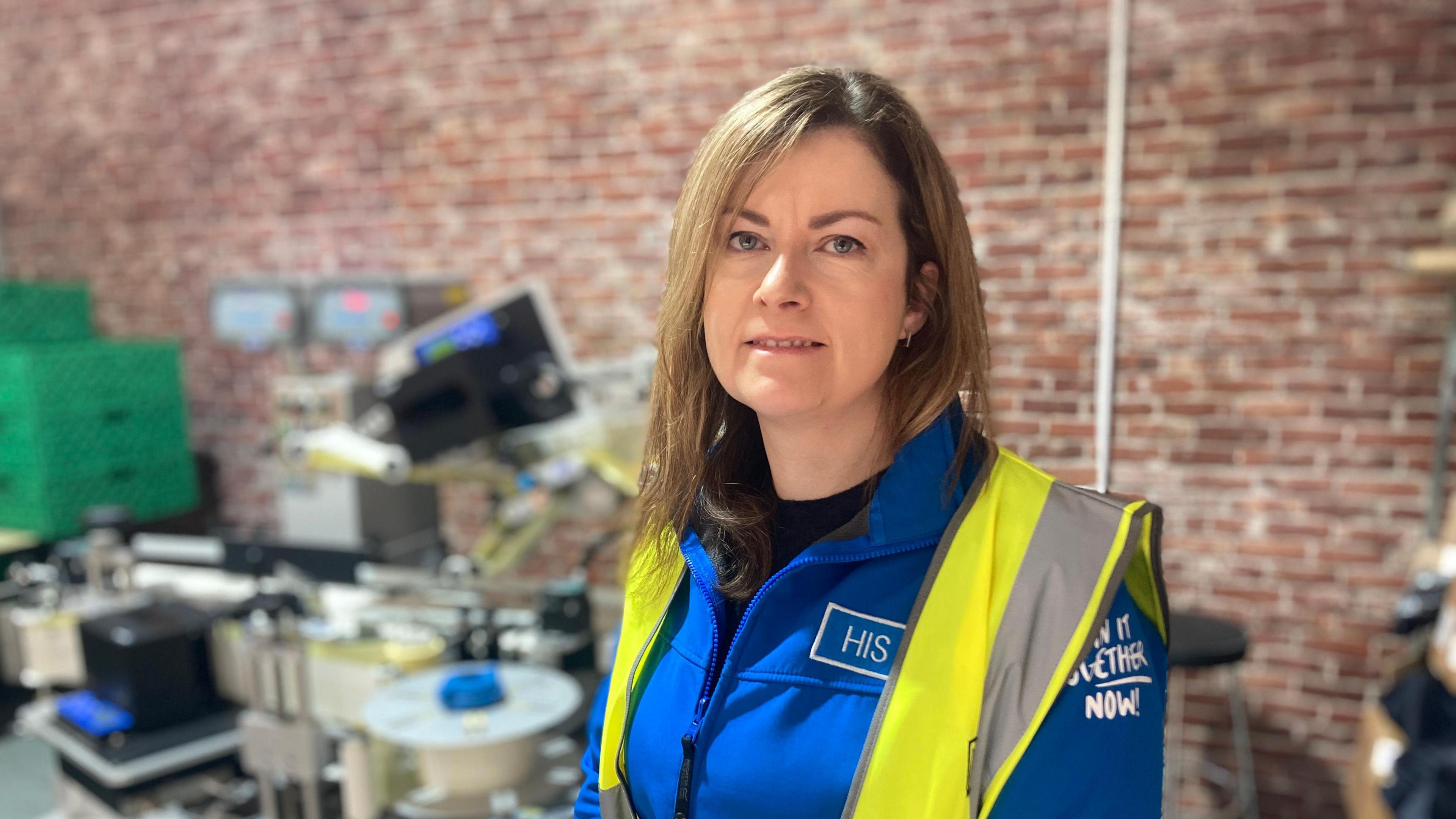 An image of Natalie Pickering. She is working in a food warehouse and wearing a blue branded jumper and high-visibility vest.