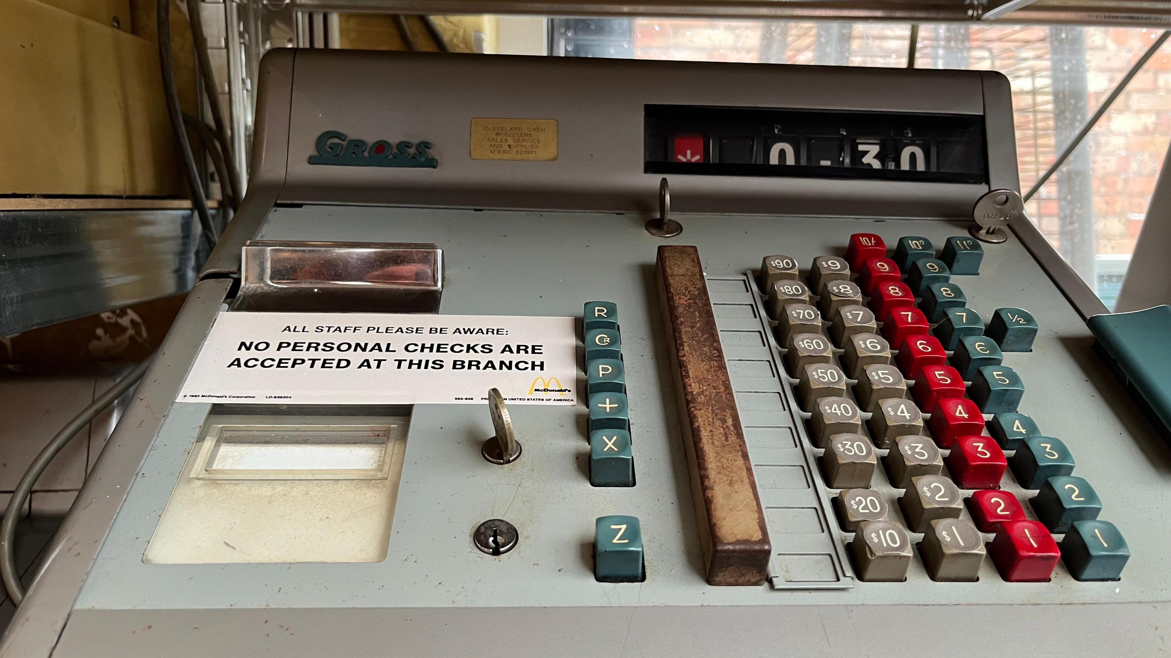 A vintage cash register, it is grey with blue, grey and red buttons 