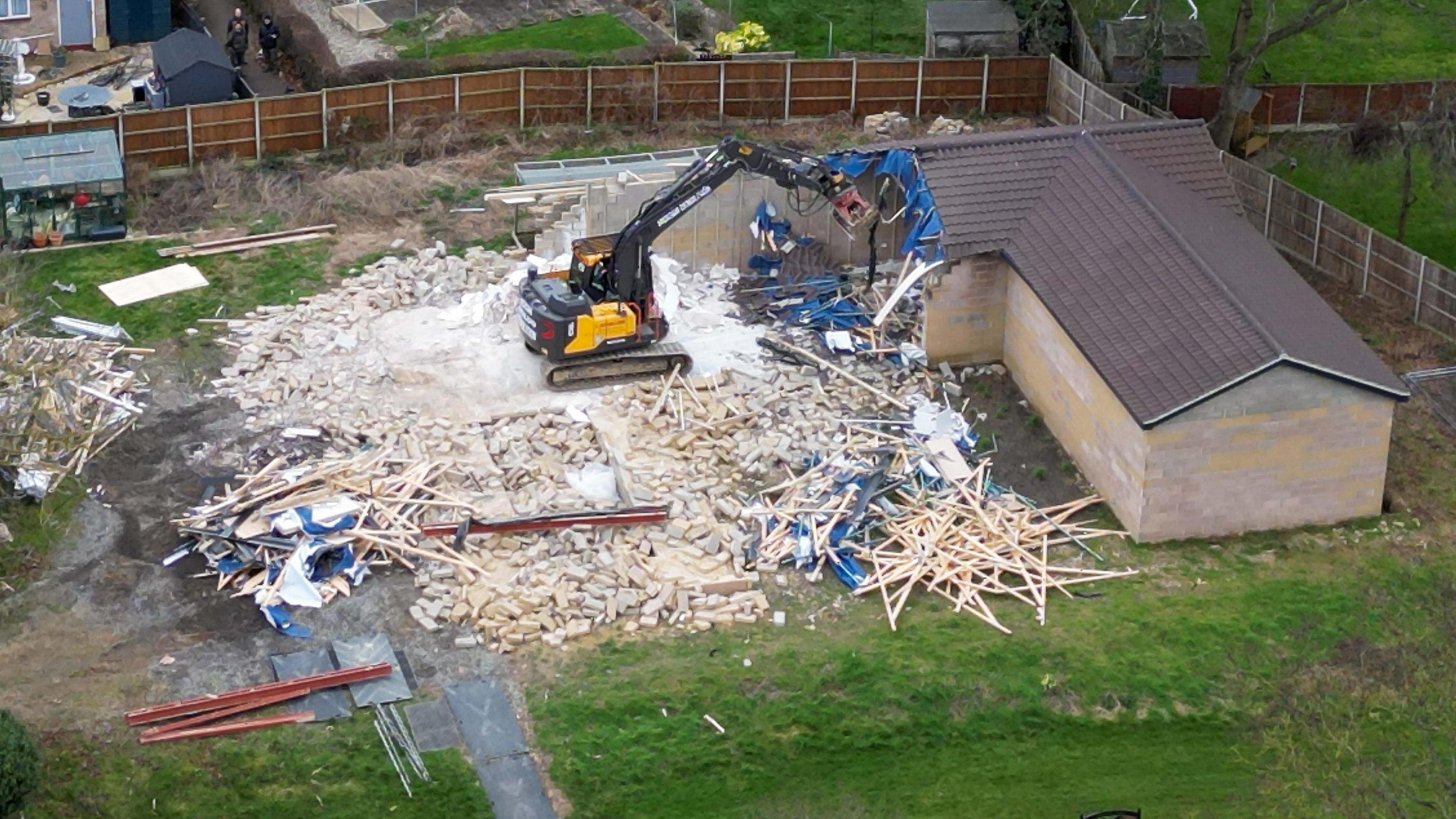 A digger demolishes the spa pool block at the home of Hannah Ingram-Moore, the daughter of the late Captain Sir Tom Moore, at Marston Moretaine, Bedfordshire. The picture is taken from above, and debris is spread across the grass