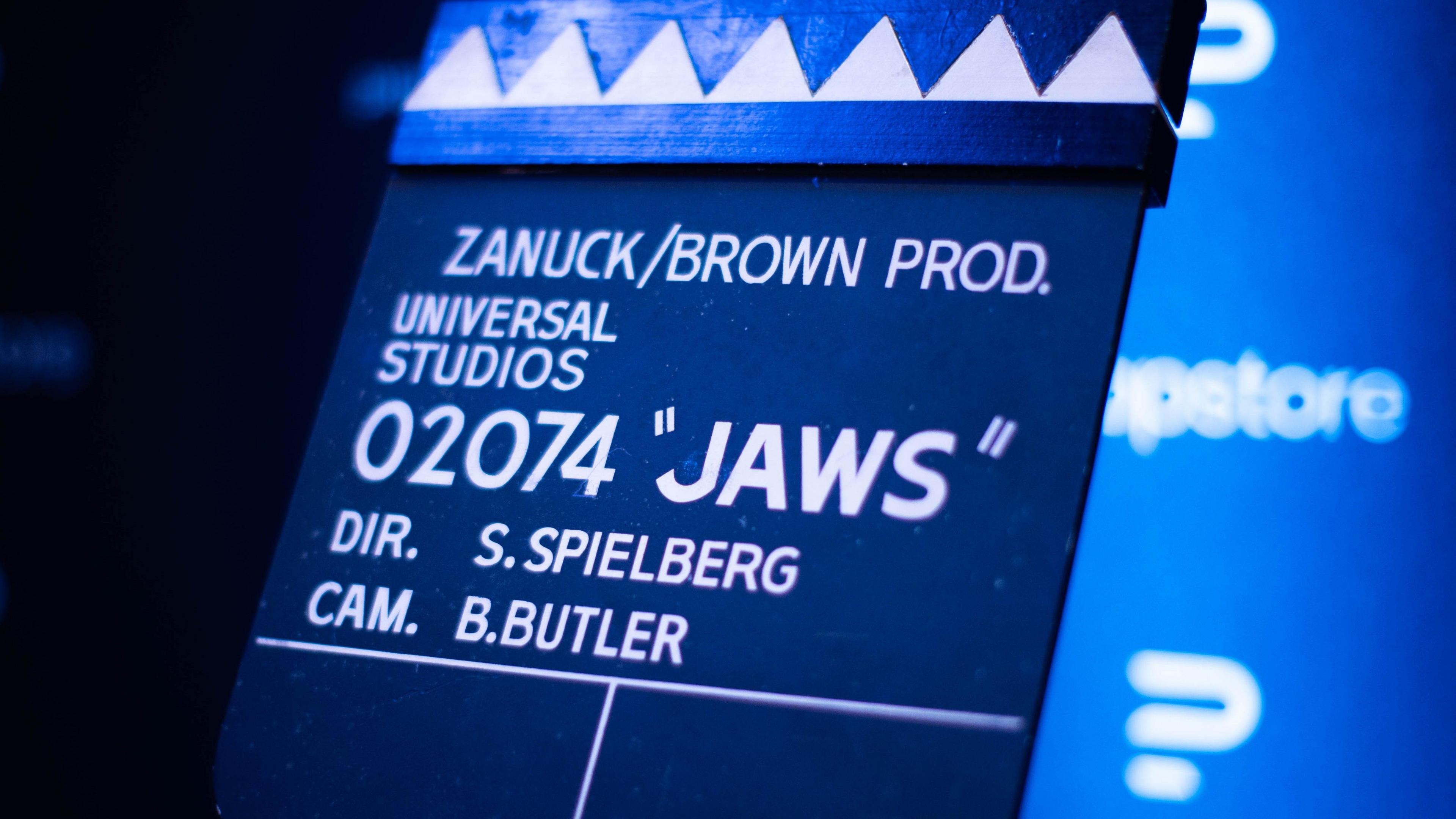 A movie clapboard with shark teeth at the top. It reads 020774 "JAWS".