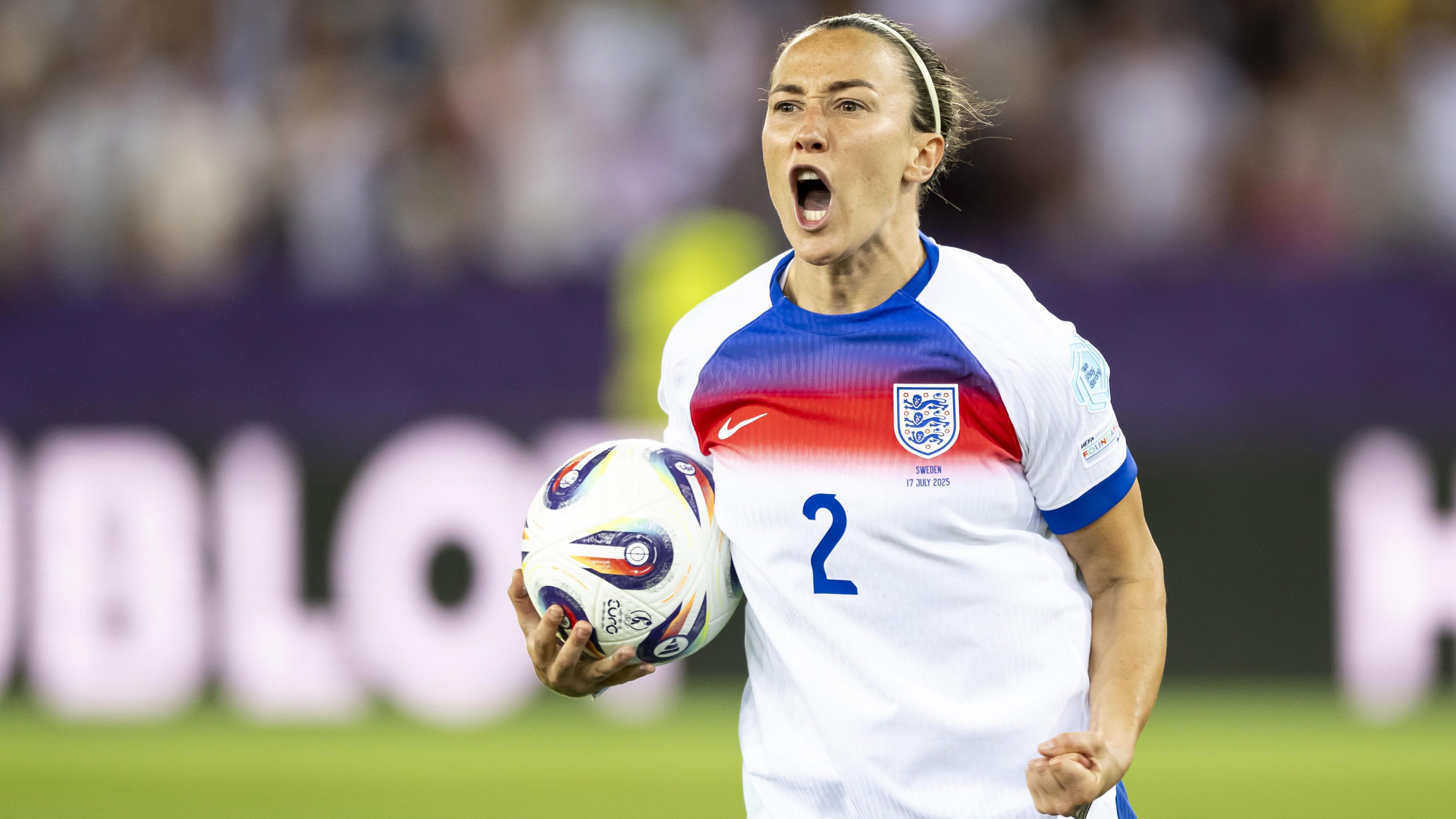 Lucy Bronze celebrates after scoring during the penalty shoot-out of the quarter-final match between England and Sweden. She is cradling the ball under her right shoulder and clenching her left fist.
