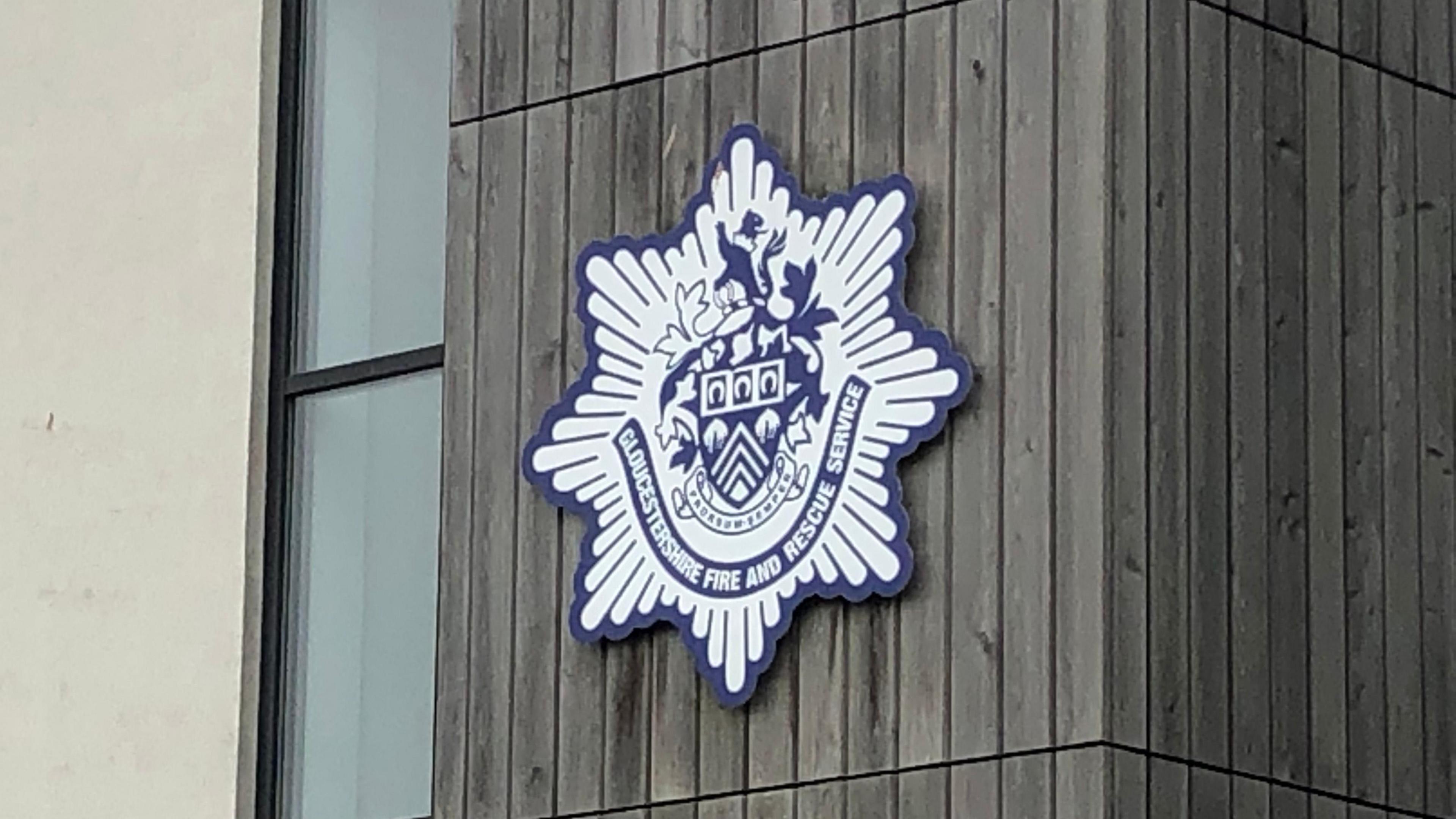 A blue and white logo showing the Gloucestershire Fire and Rescue Service crest on a building.