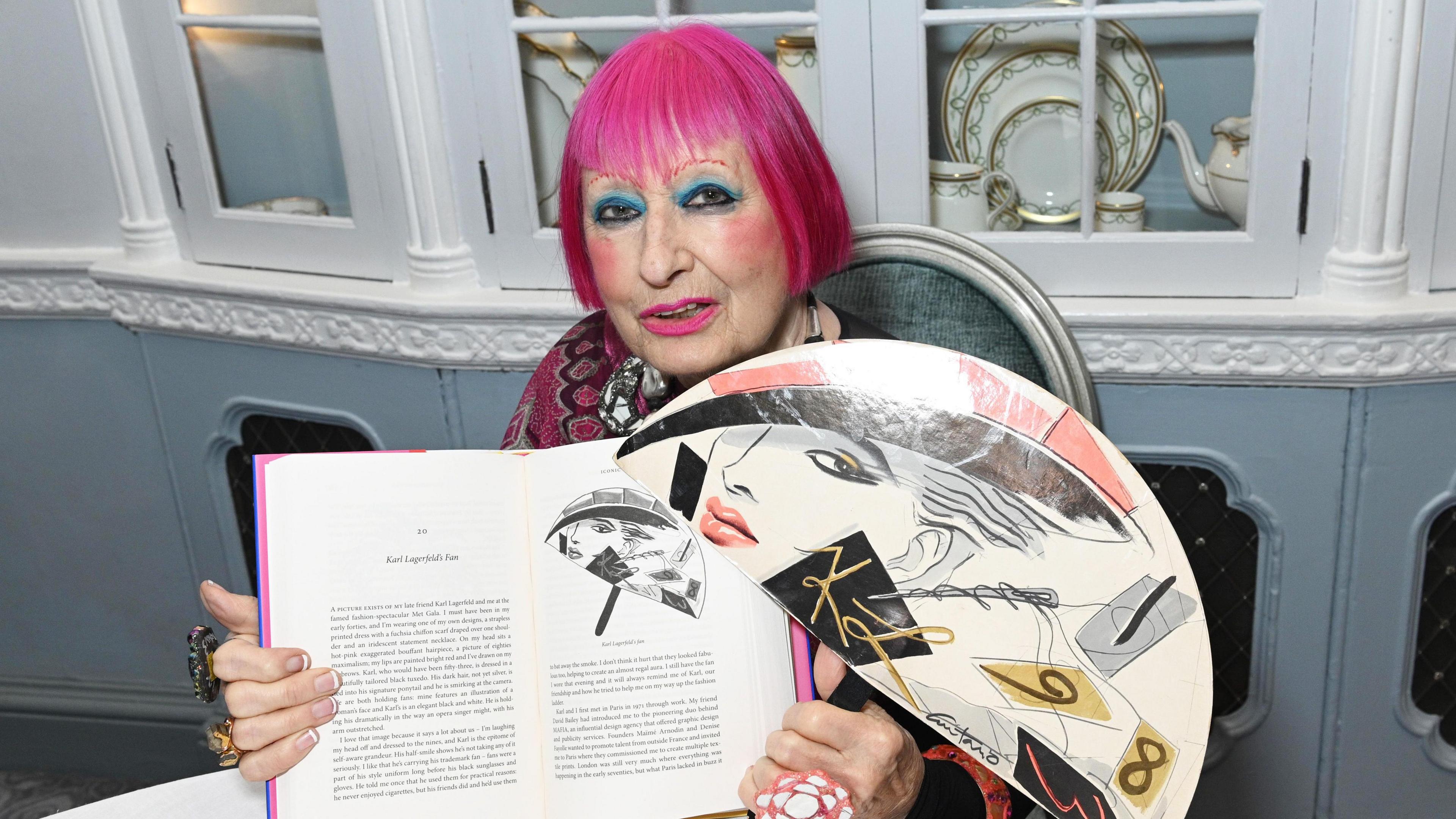 Dame Zandra Rhodes holding up her book Iconic