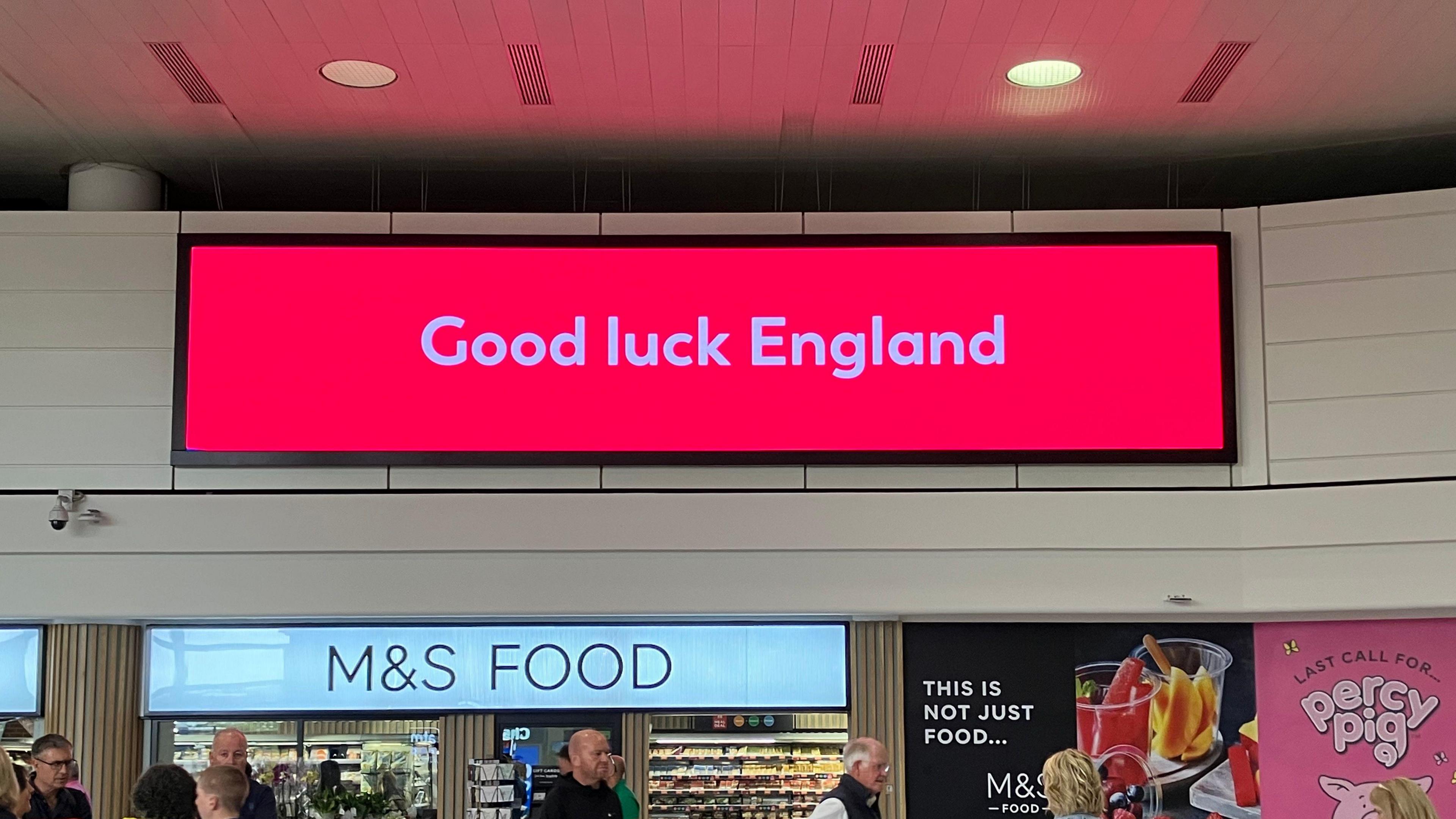 A large red electronic sign at Gatwick Airport, reading Good Luck England in white text