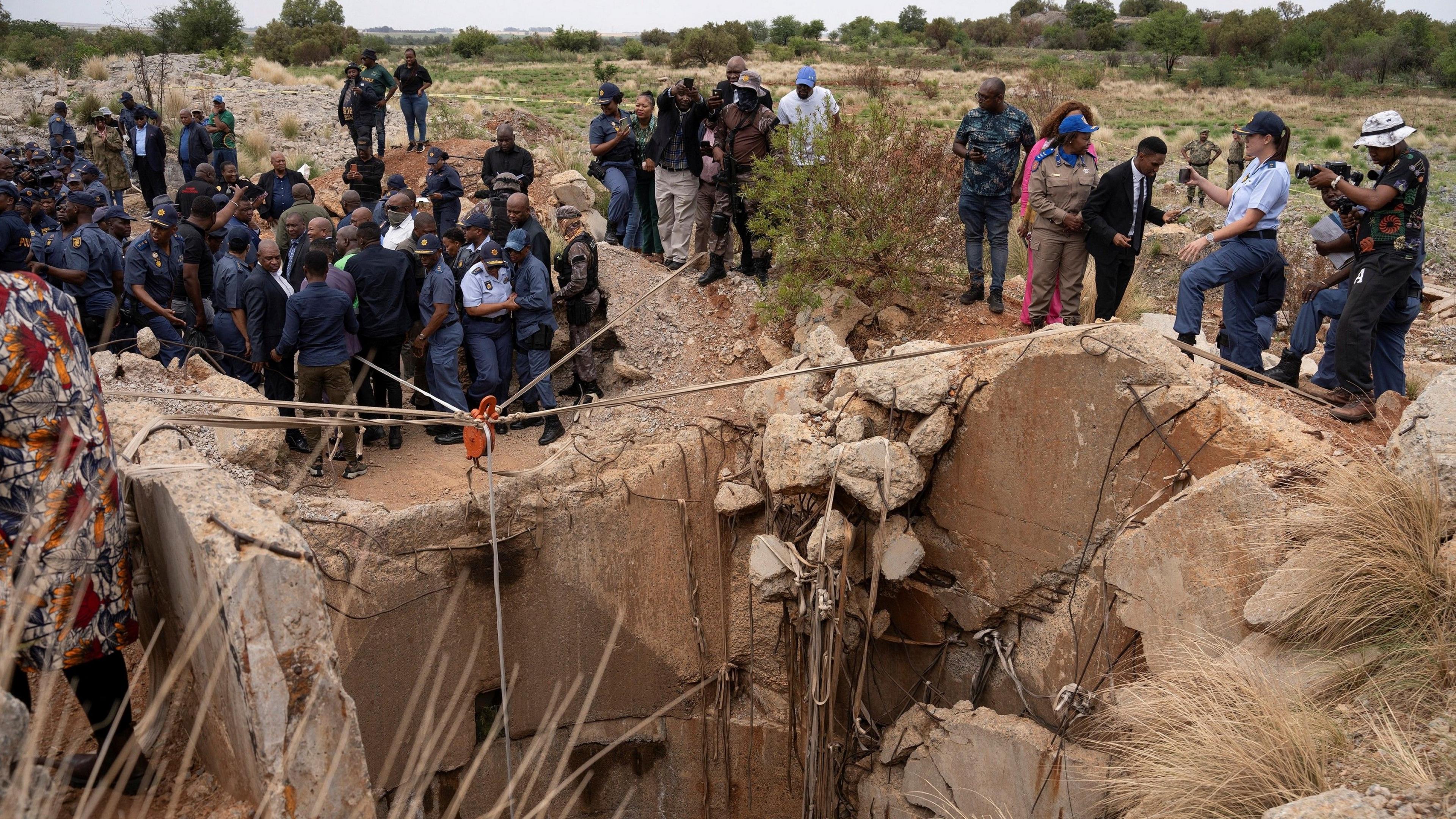 Community members watch as Senzo Mchunu, South African police minister, inspects outside the mineshaft where it is estimated that hundreds of illegal miners are believed to be hiding underground.