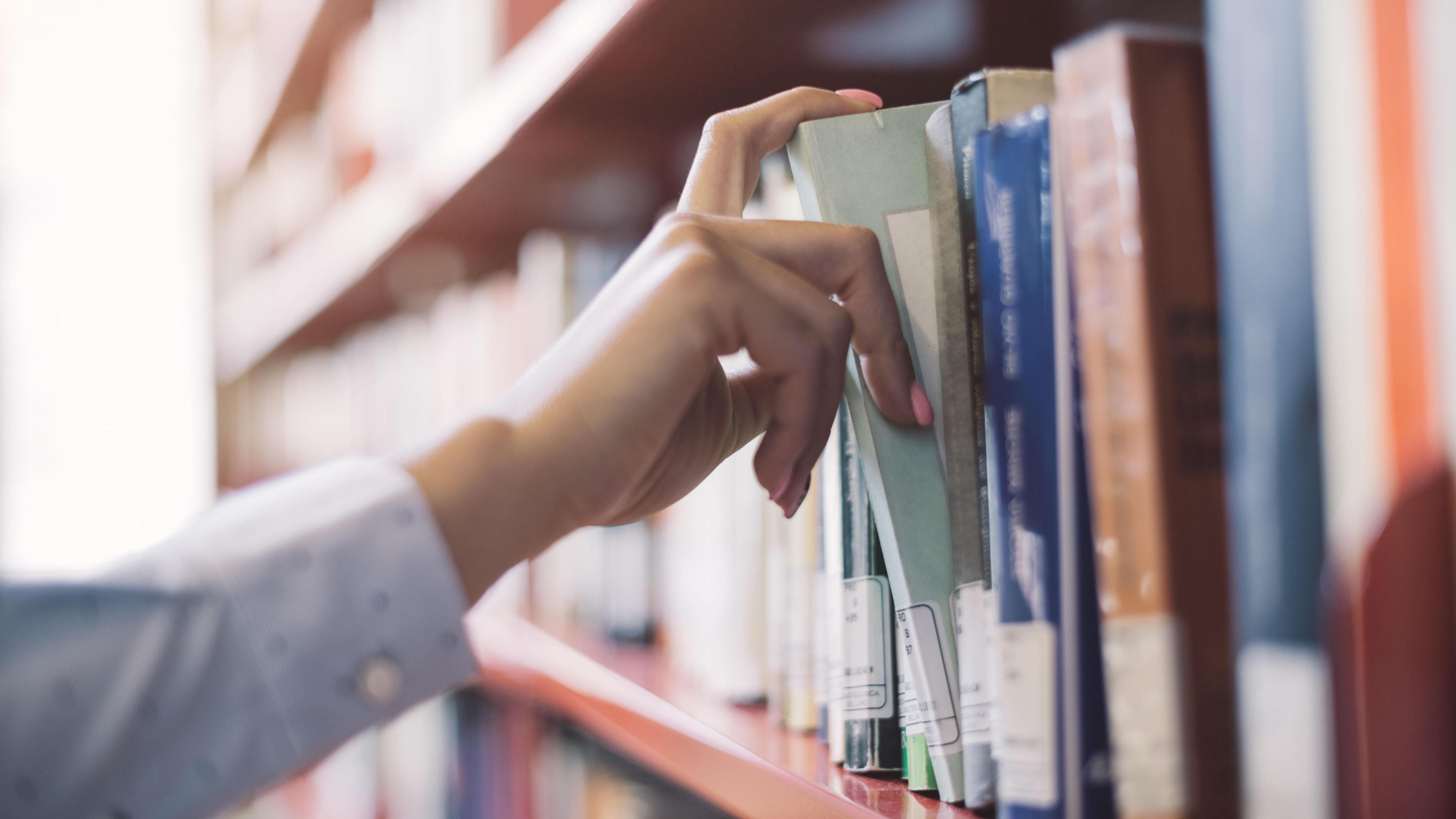 A hand picking a book from a bookshelf