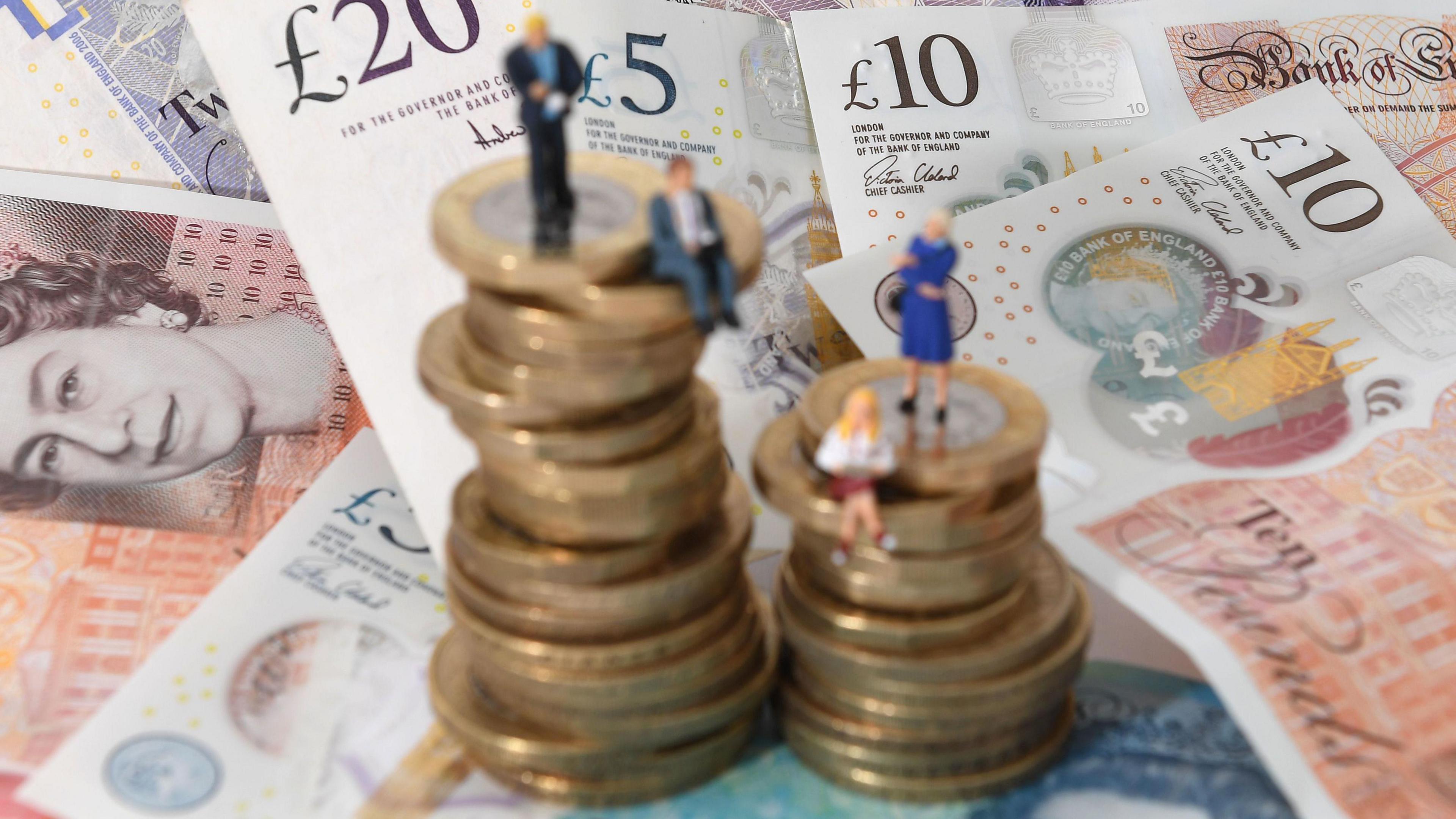 Models of men and women on a pile of coins and bank notes.