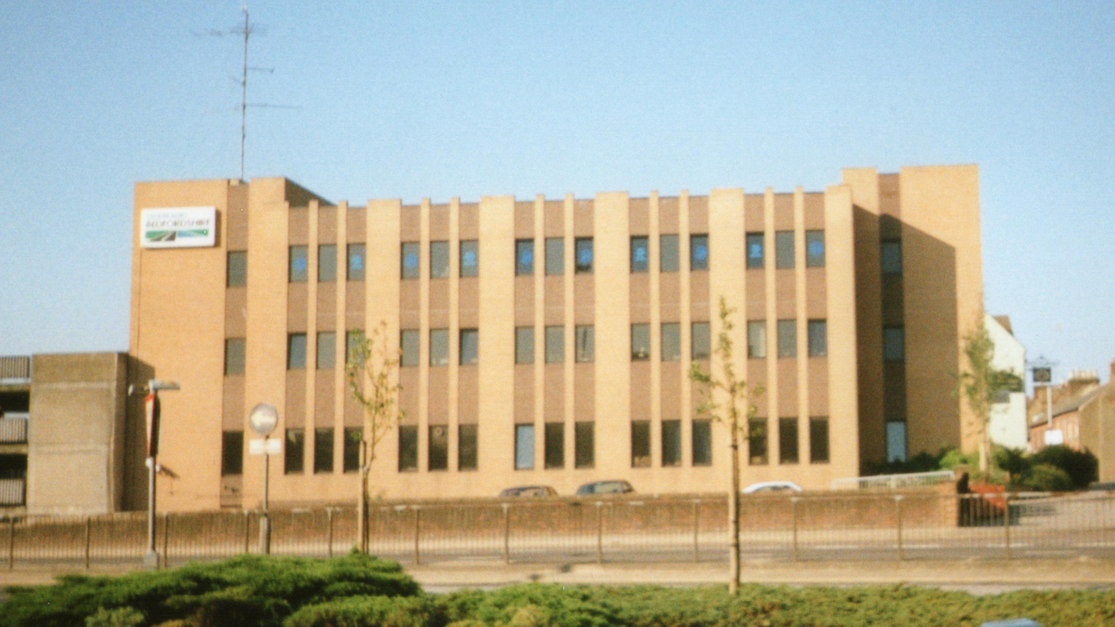 The large cream-coloured building that once housed Radio Bedfordshire. It has lots of windows and is about three storeys tall. It faces onto a road and has a large antenna on the roof.