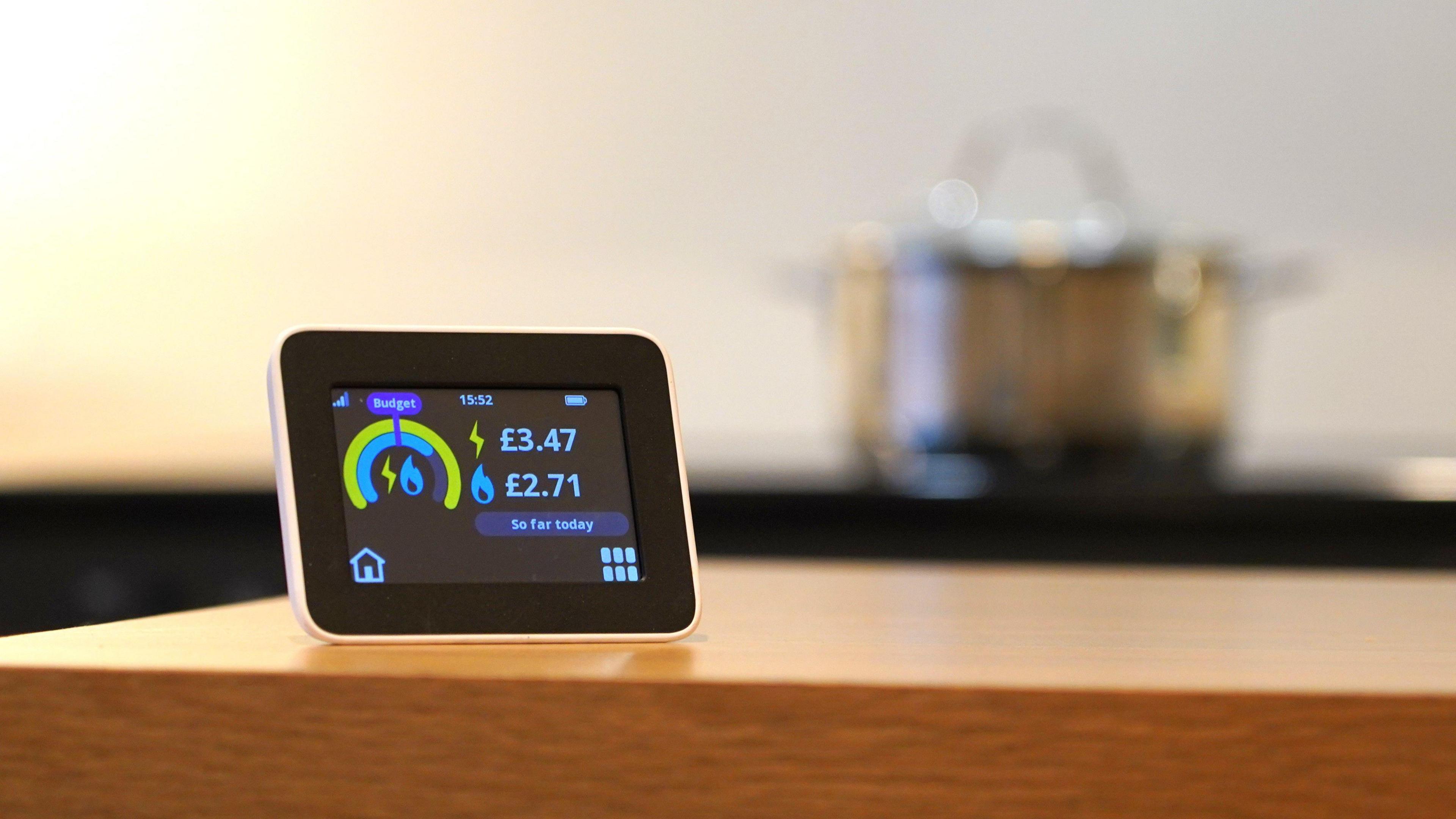 Electricity smart meter on a kitchen counter with a pot on a stove in the background.