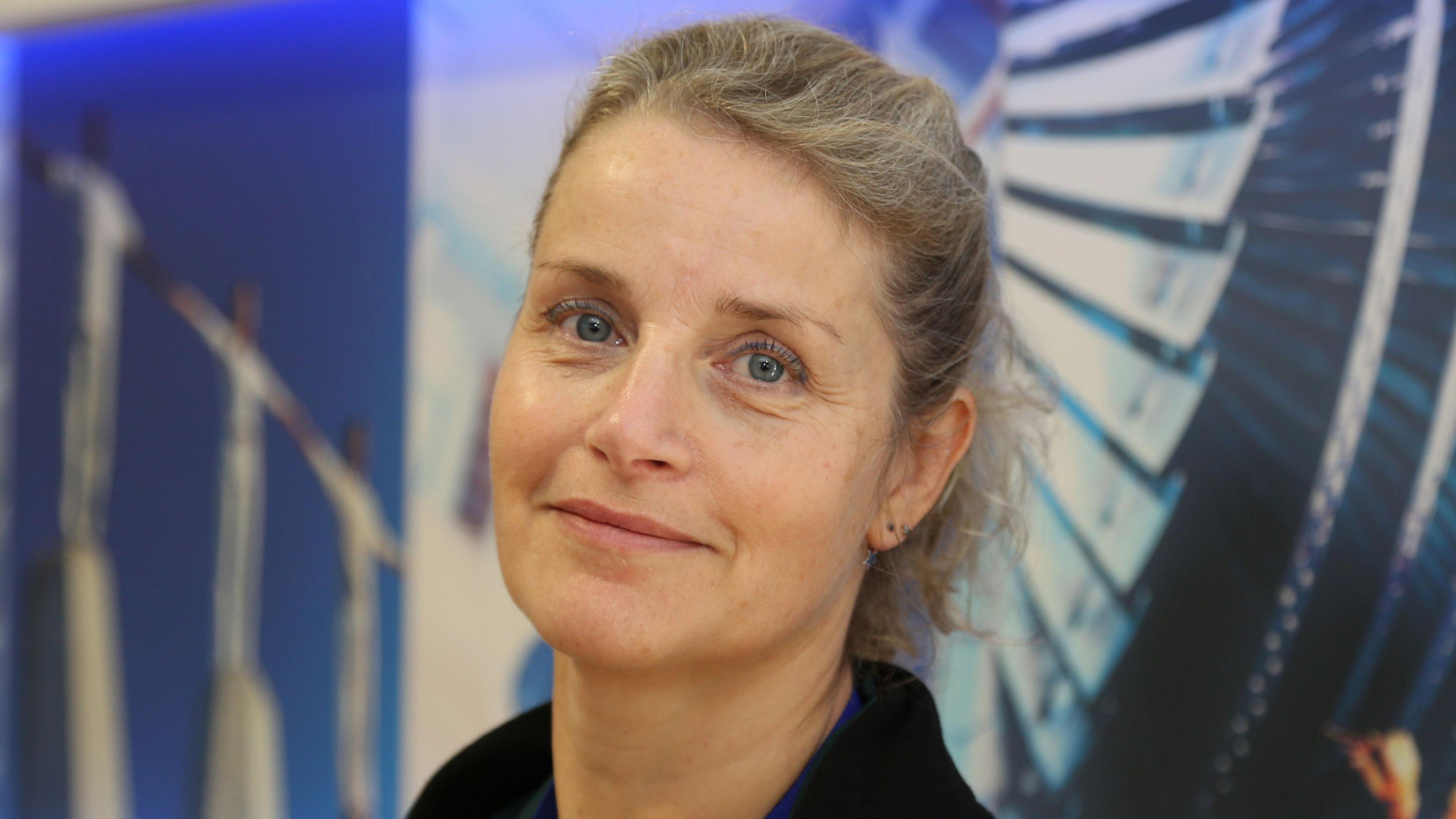 This is a close up shop of Diana staring and smiling directly into the camera.
She is standing infront of a blue and white backdrop.