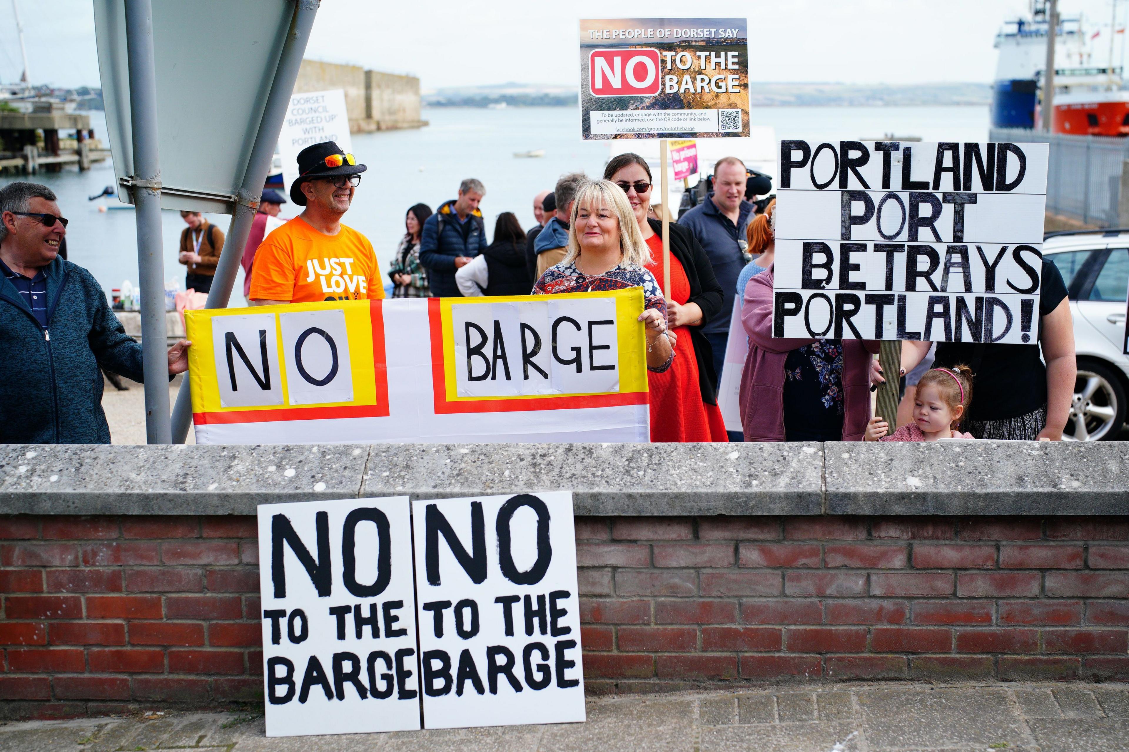 Protestors stand in front of Portland docks with placards with slogans including 'No to the barge' and 'Portland Port betrays Portland'