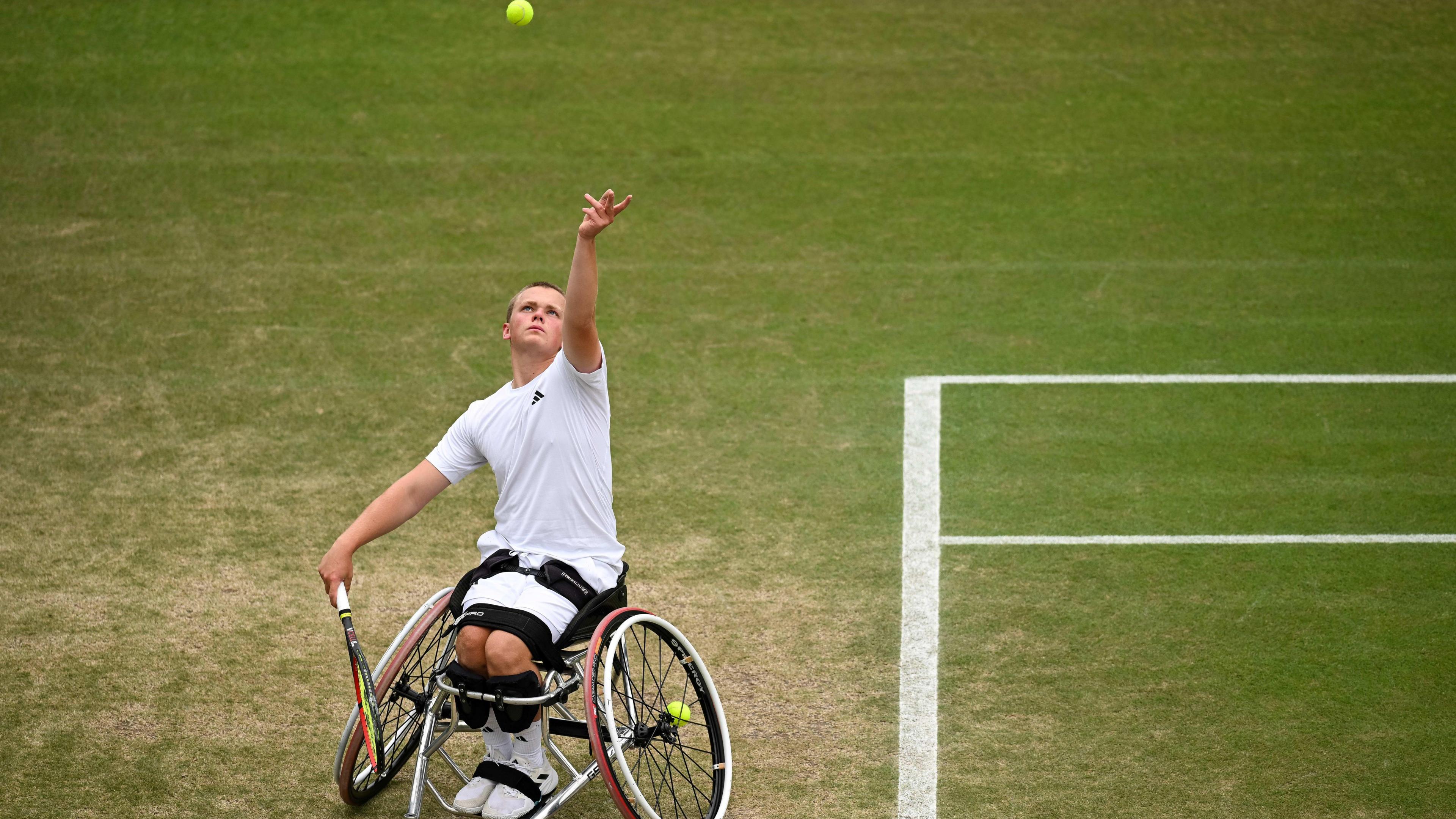 Wheelchair tennis star Ben Bartram tosses the ball up to serve on a grass court