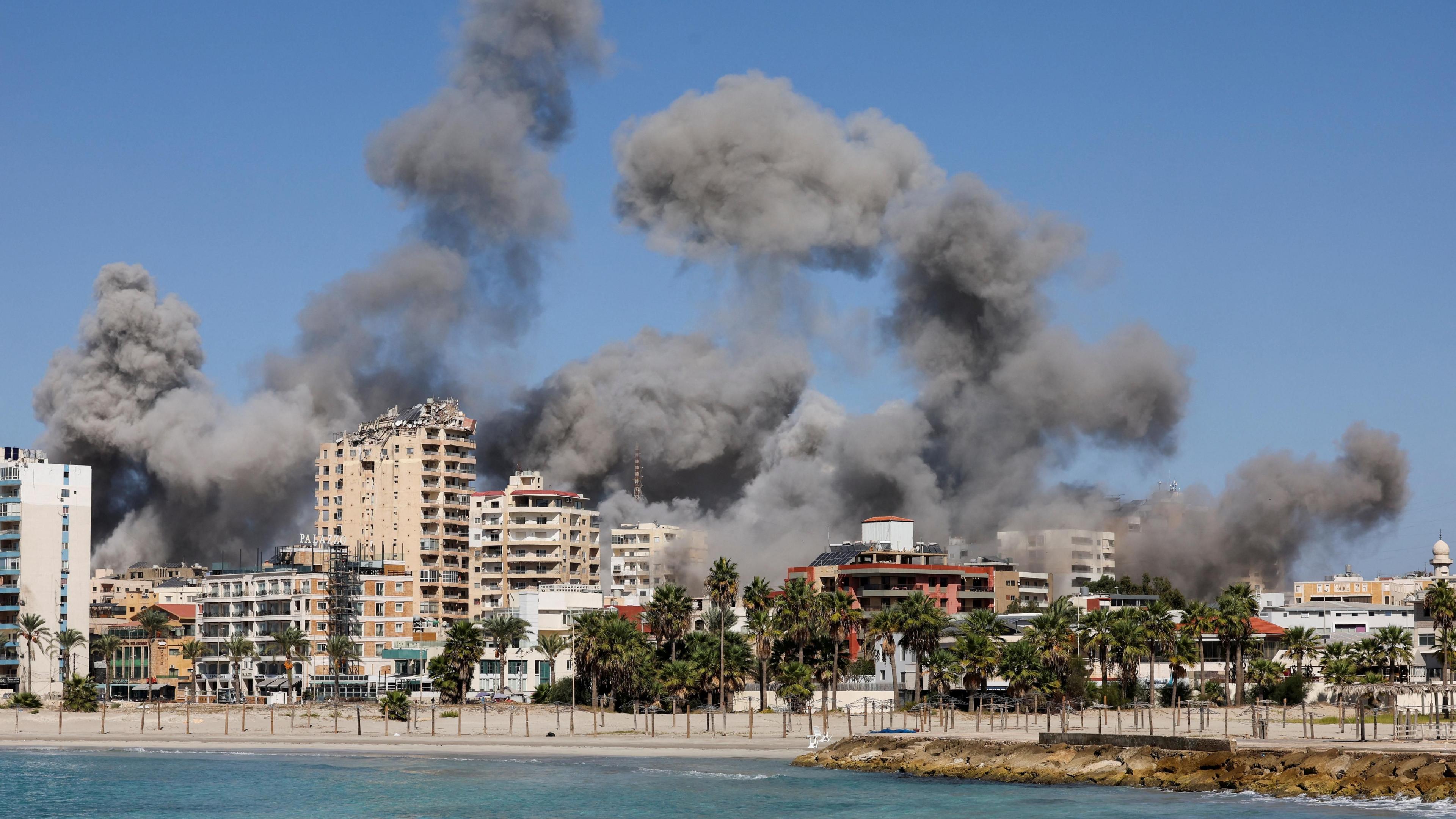 Smoke billows after Israeli strikes in the southern Lebanese city of Tyre (23 October 2024) - the coast of Tyre is visible from the water, with a number of mid-sized tower blocks and trees visible on Tyre's beach.