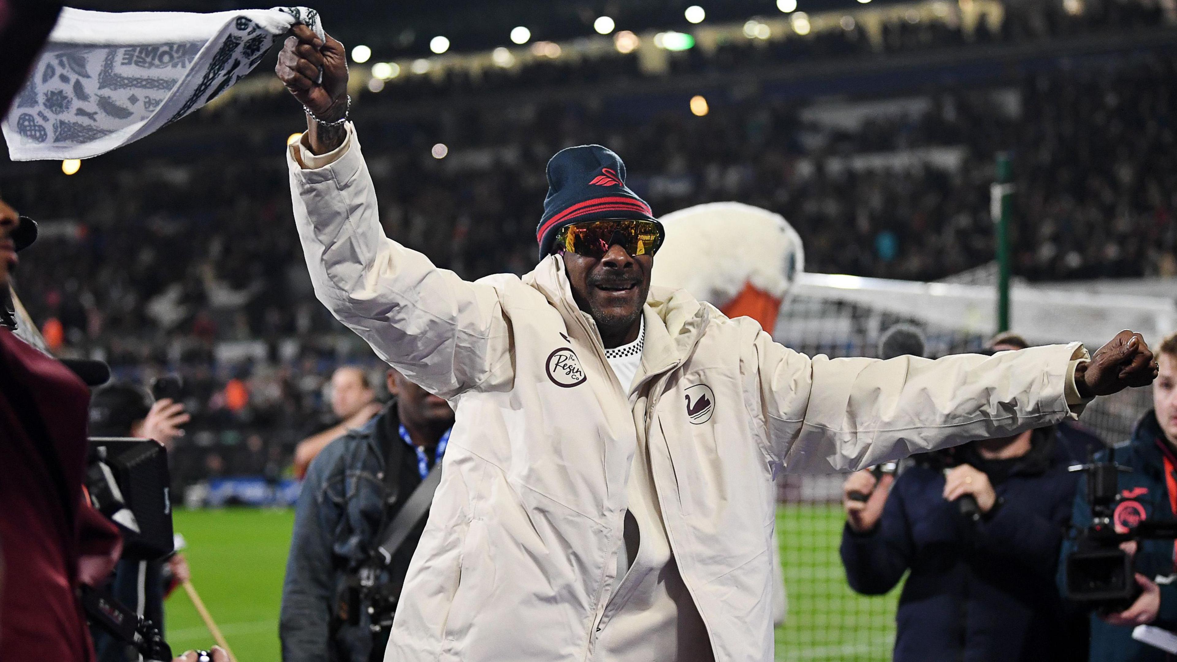 Snoop Dogg waves a branded towel in front of fans at the Swansea.com Stadium