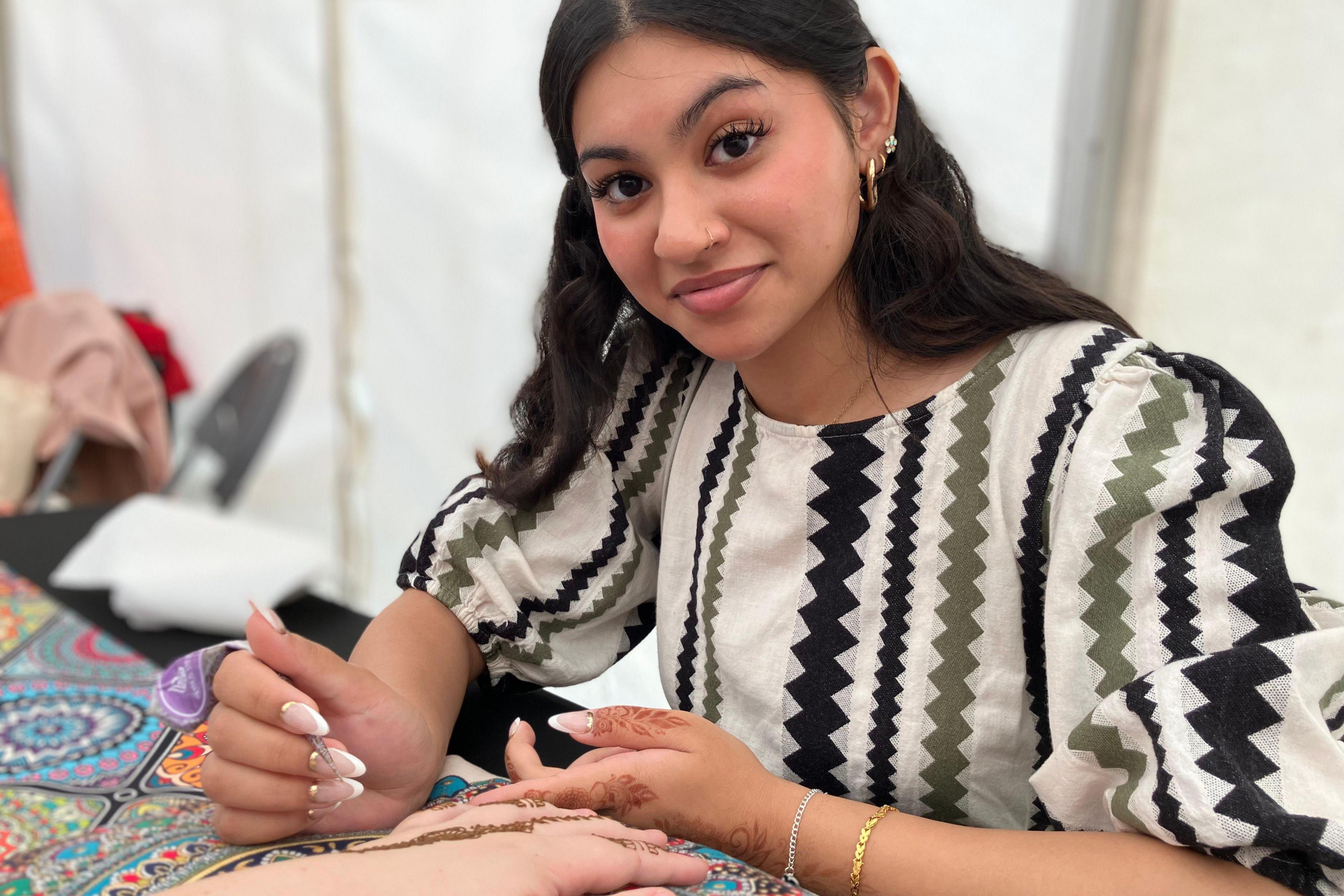 A woman is painting a henna tattoo on another woman's hand