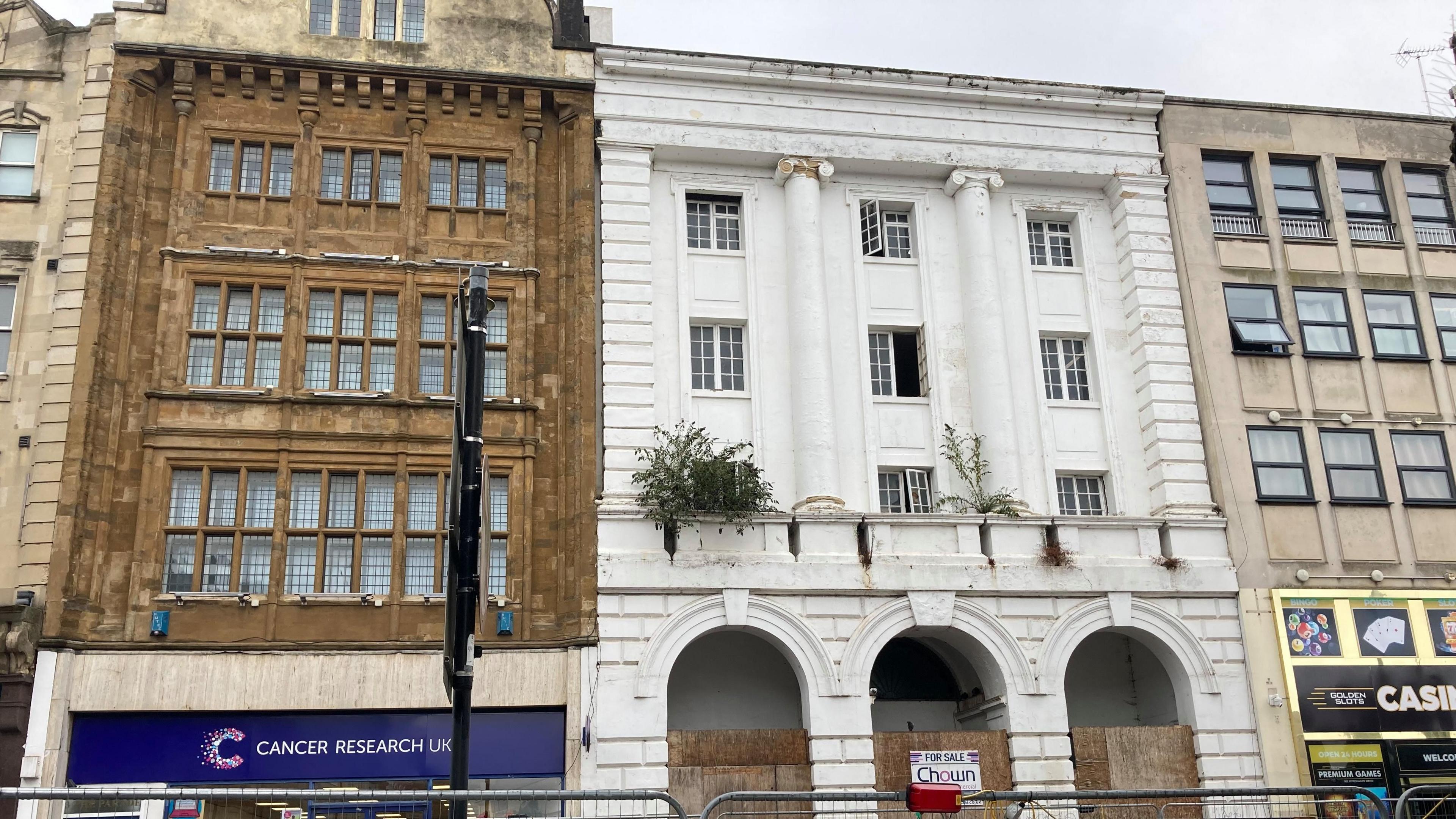 The Corn Exchange, a white Grade II listed building. At the front of the building are three archways, which are partially boarded up. The building has a Cancer Research on one side and a casino on the other. 