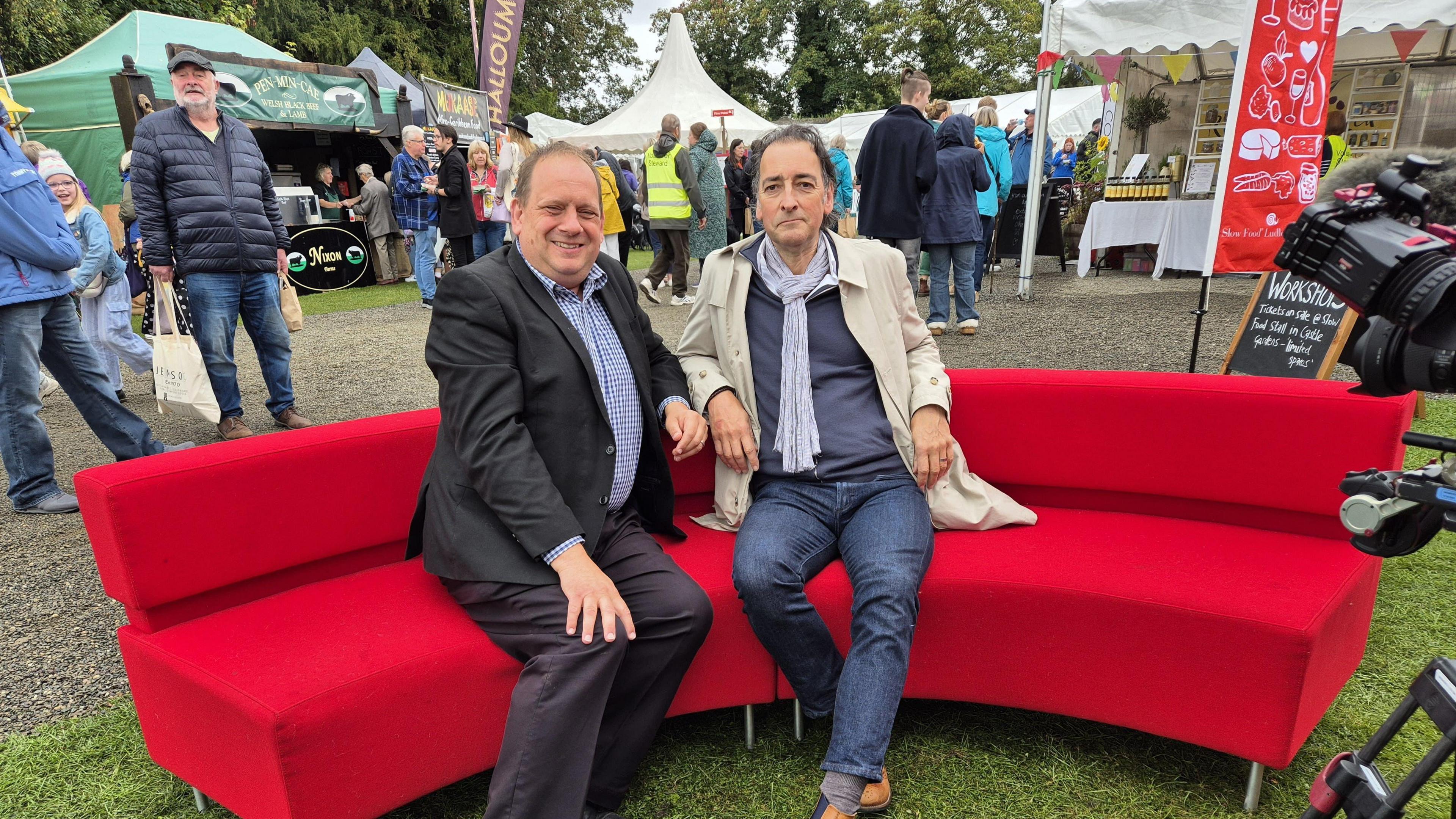 Reporter Ben Sidwell sitting on red sofa with the impressionist Alistair McGowan at Ludlow Food Festival