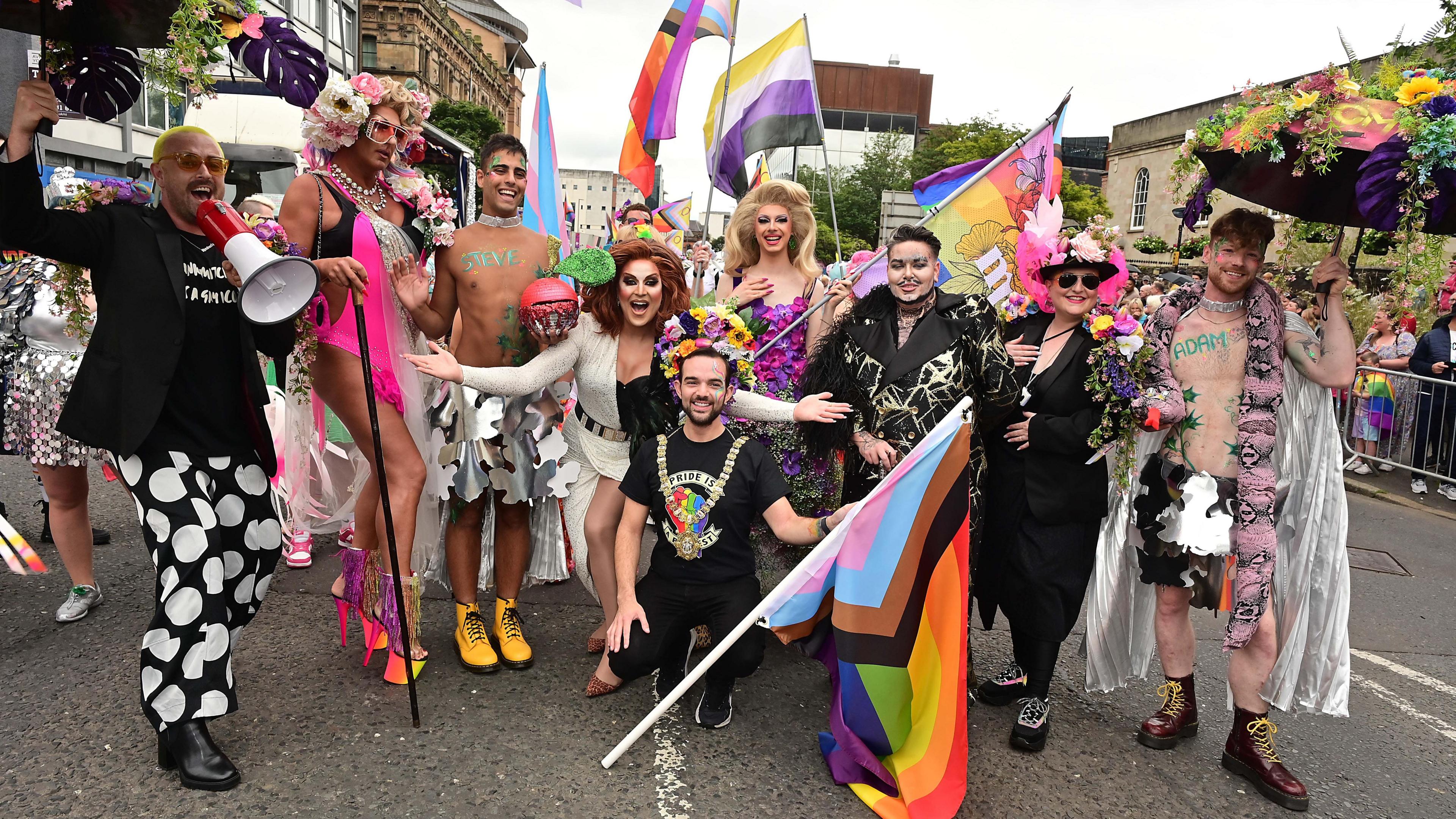 Nicky Murray wearing his mayoral chain and a t-shirt that reads "pride is protest" leading the parade whilst carrying a pride flag