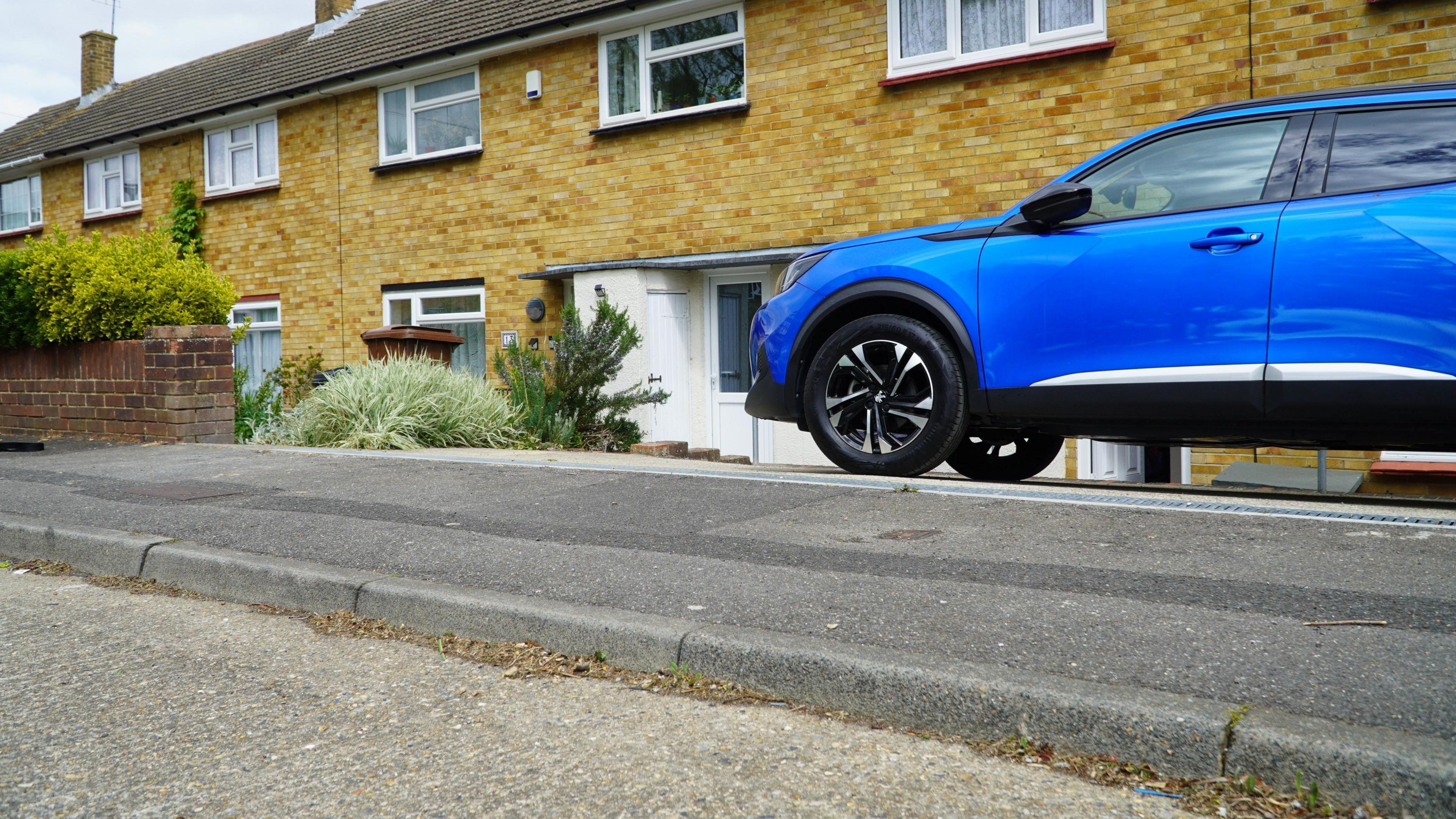 A view from the ground up of the kerb, with Mr Partridge's blue car parked on the pavement.