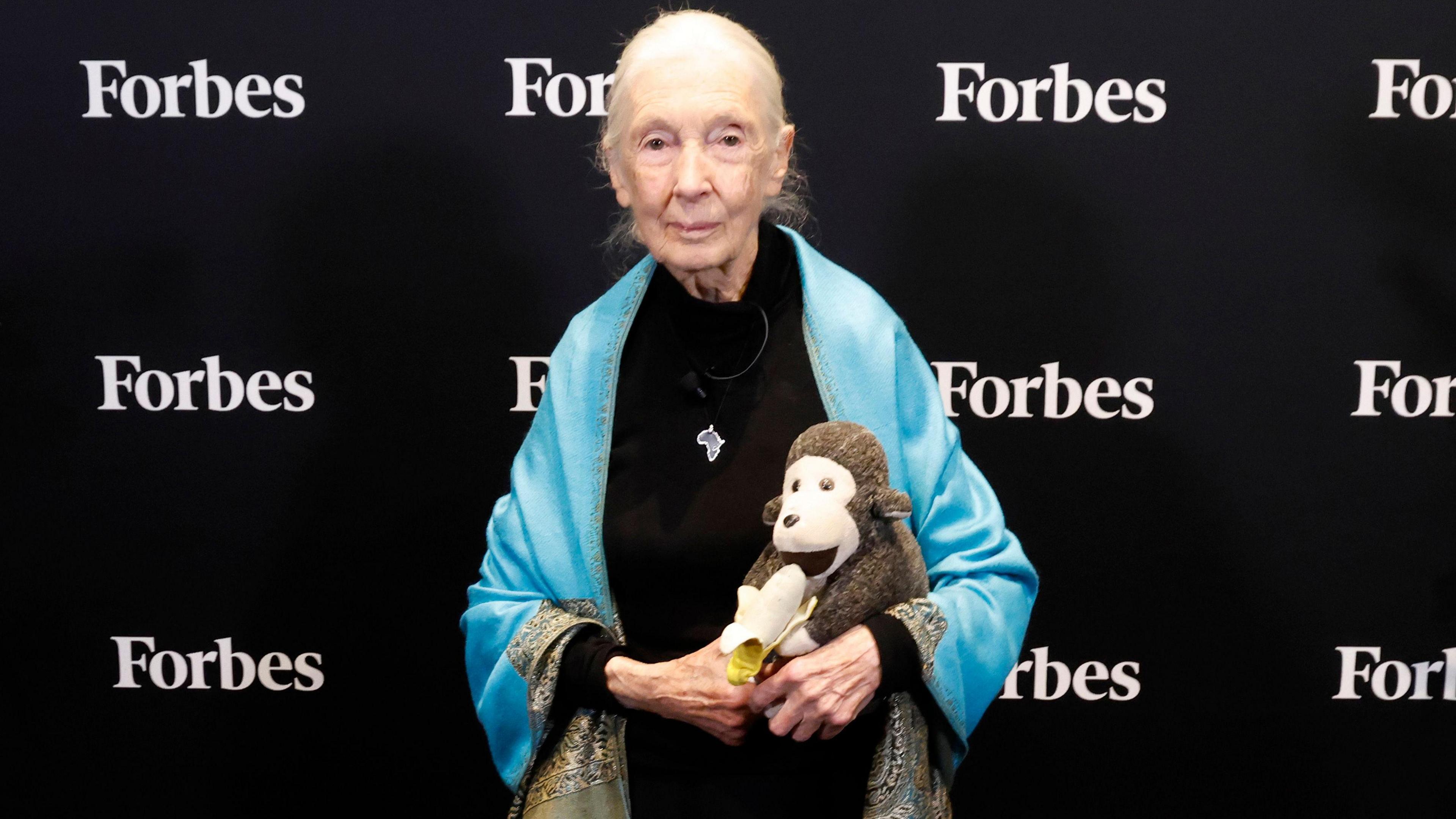 Jane Goodall appears in front of the Forbes logo holding a toy monkey and banana in her hands.