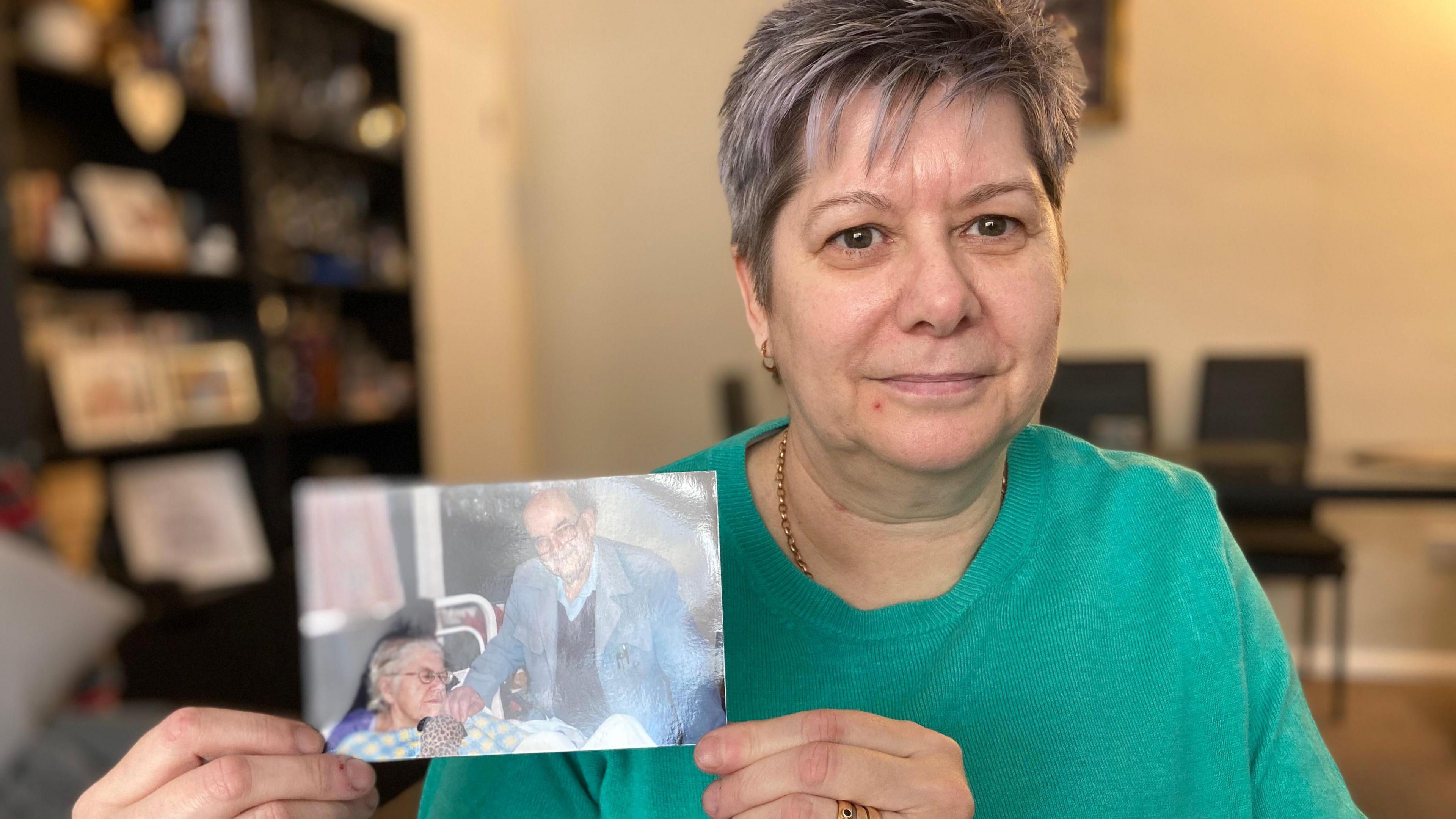 Molly Phew looks at the camera wbile holding up a photograph of her father, John who died during the Covid pandemic 