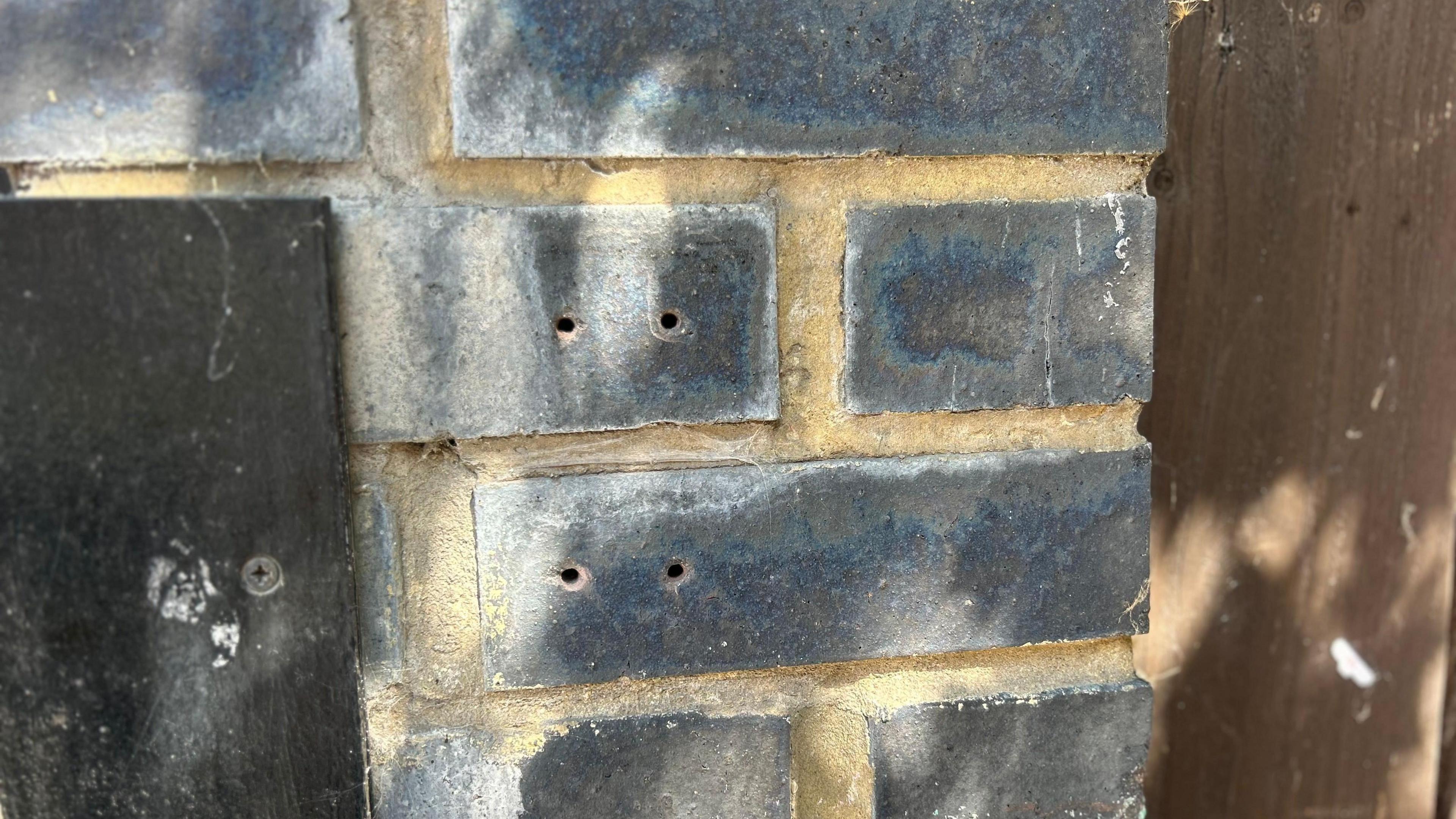 A grey wall outside a home with holes in the wall where a lockbox used to be 