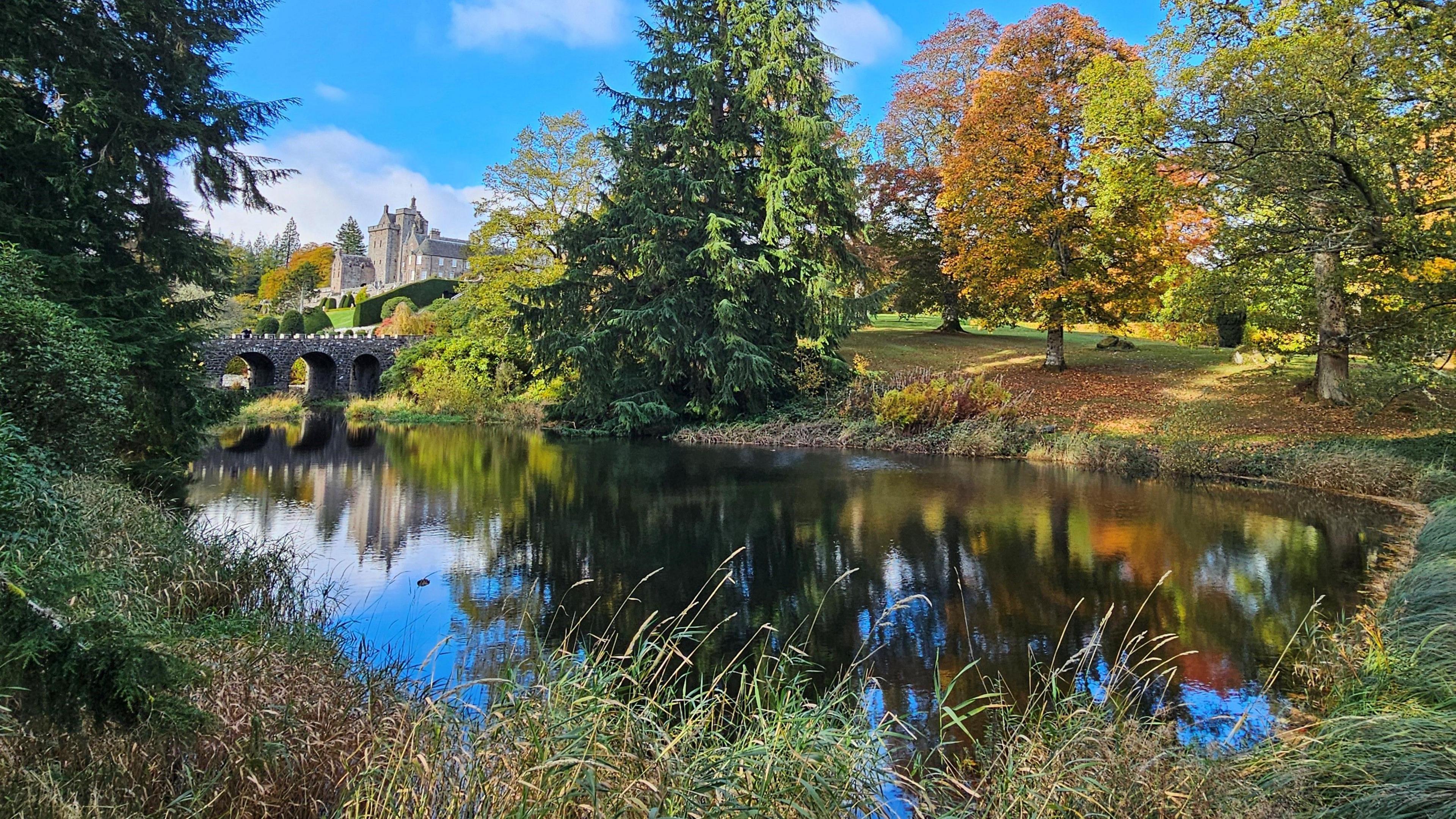 There is a river with reflections of the colourful trees that are on the banks. the sky is blue.