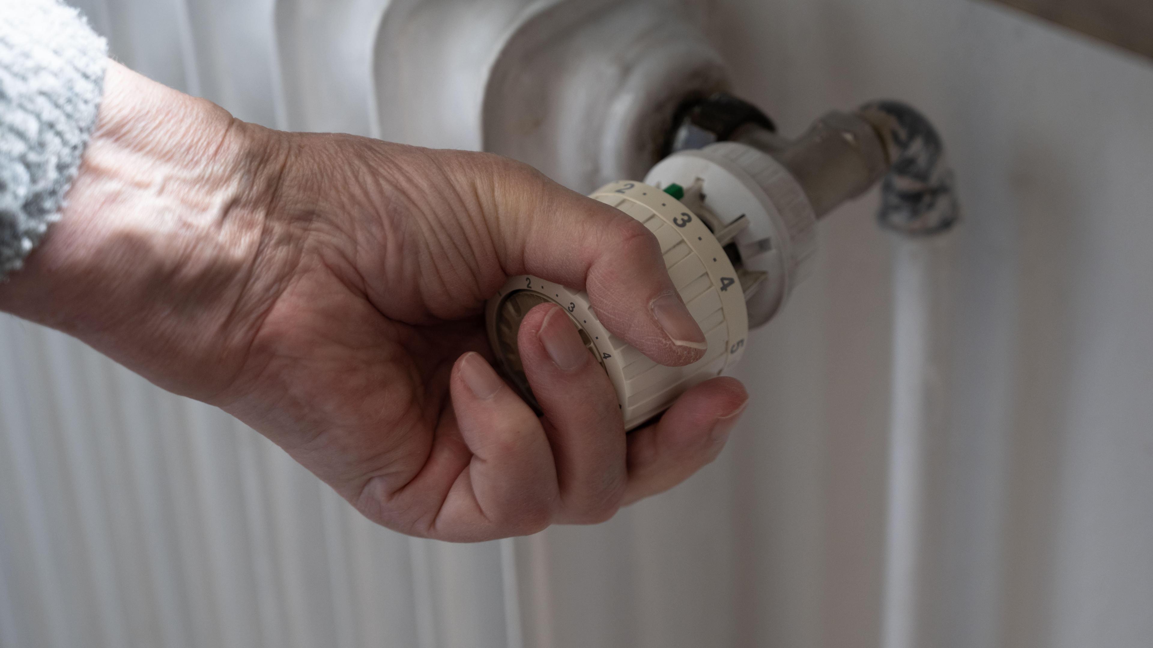 An older person's hand turning the knob on a radiator.