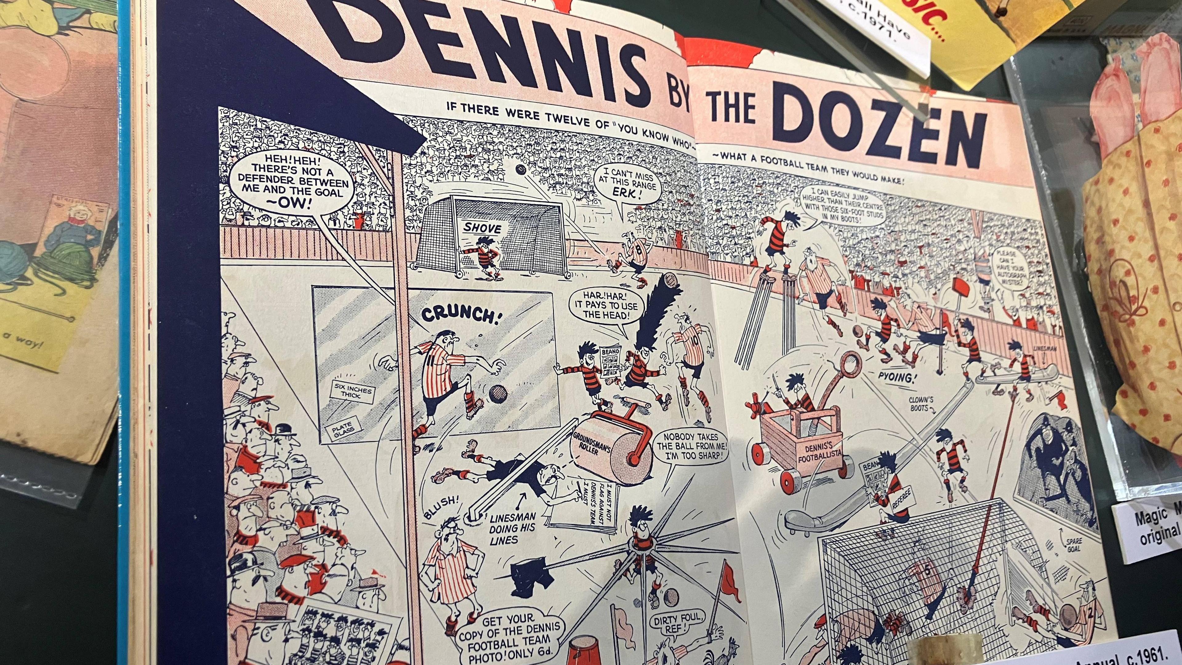 A Dennis the Menace annual from 1961 - text at the top of the double page spread in the annual reads "Dennis by the Dozen". Below it is a Dennis the Menace cartoon of a football match.