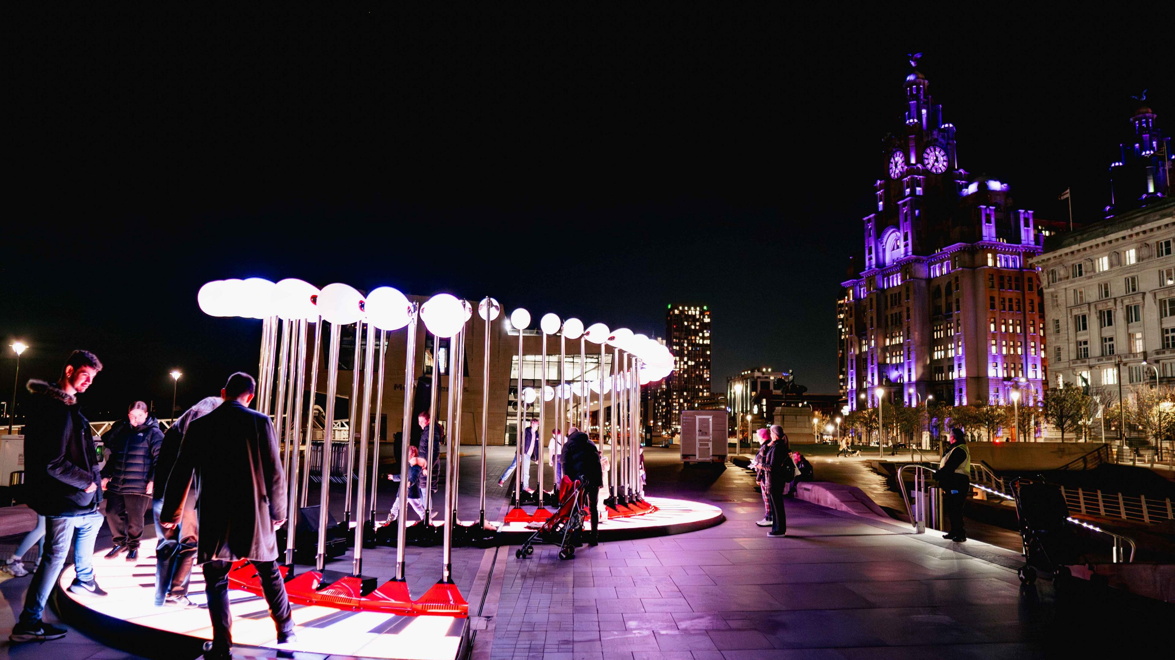 People see and stand on a piano-themed artwork in front of the Liverpool land mark buildings on the Pier Head