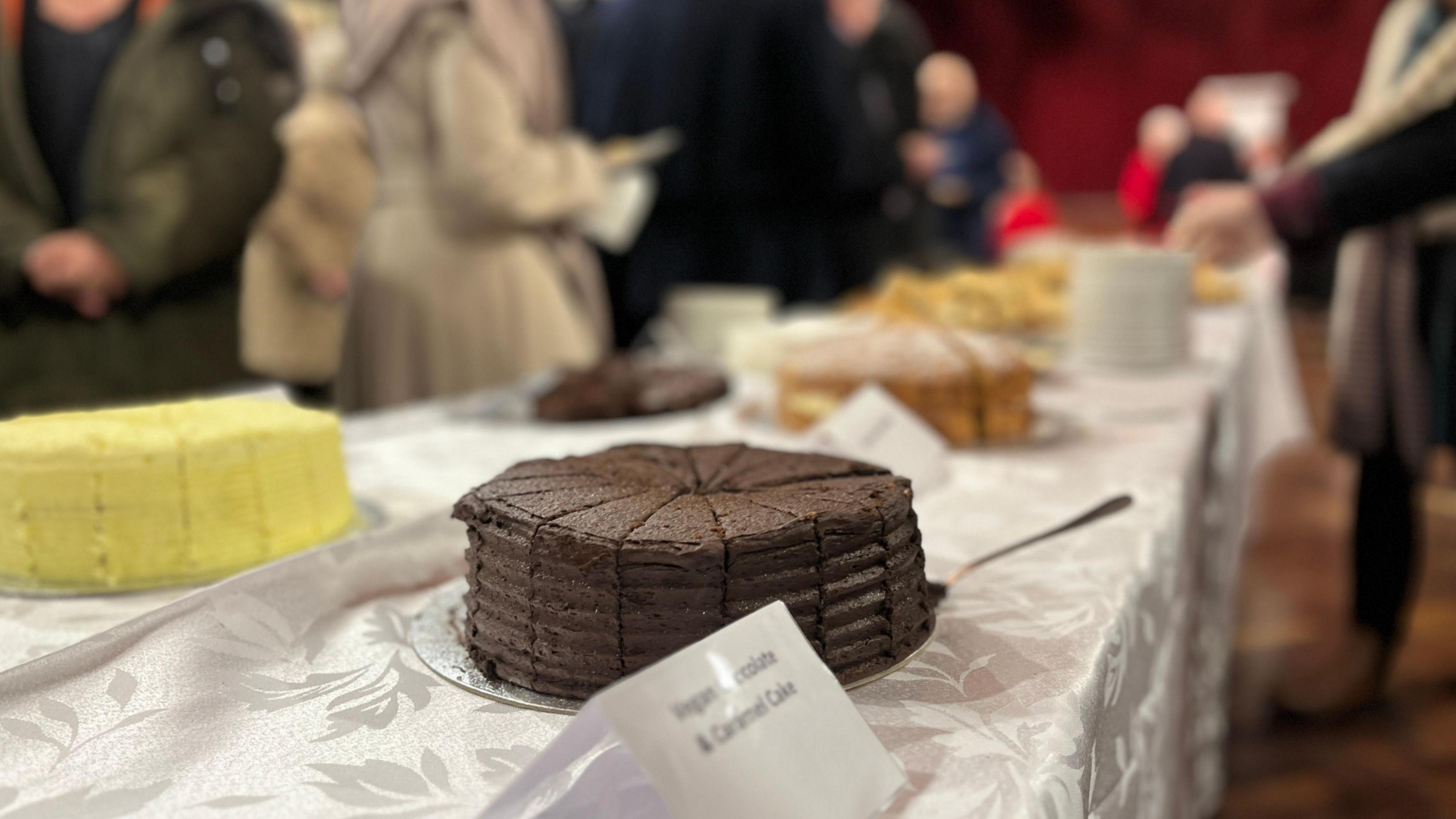 A chocolate cake on a table. Other cakes are on the table in the background.