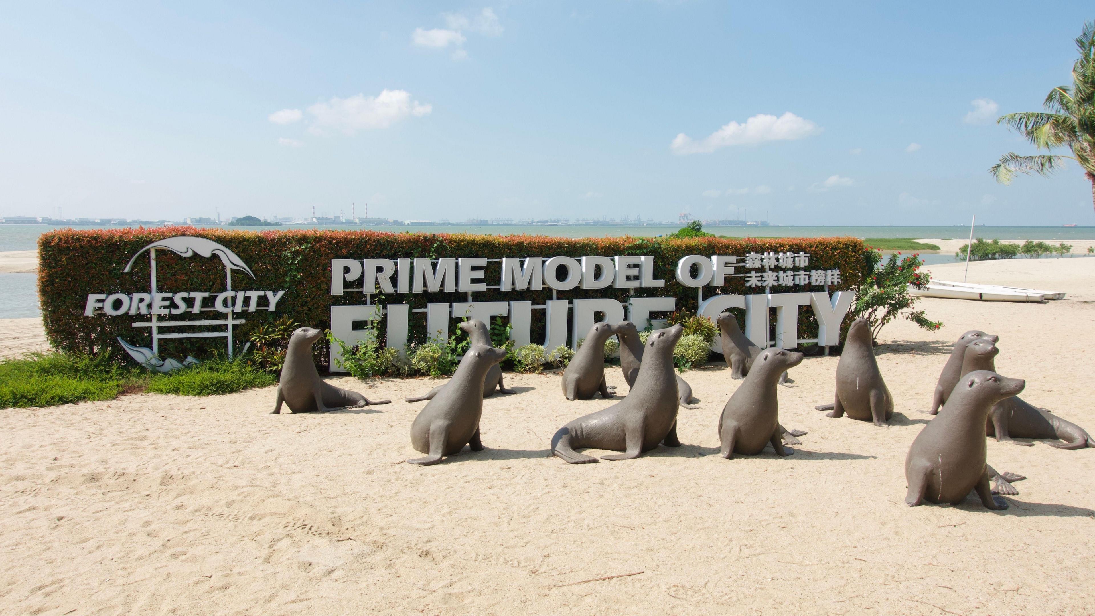 Twelve seal statues on a each in front of a hedge sporting a white "Forest City" logo and the words "Prime model of future city" in all capitals. Ocean in the background.