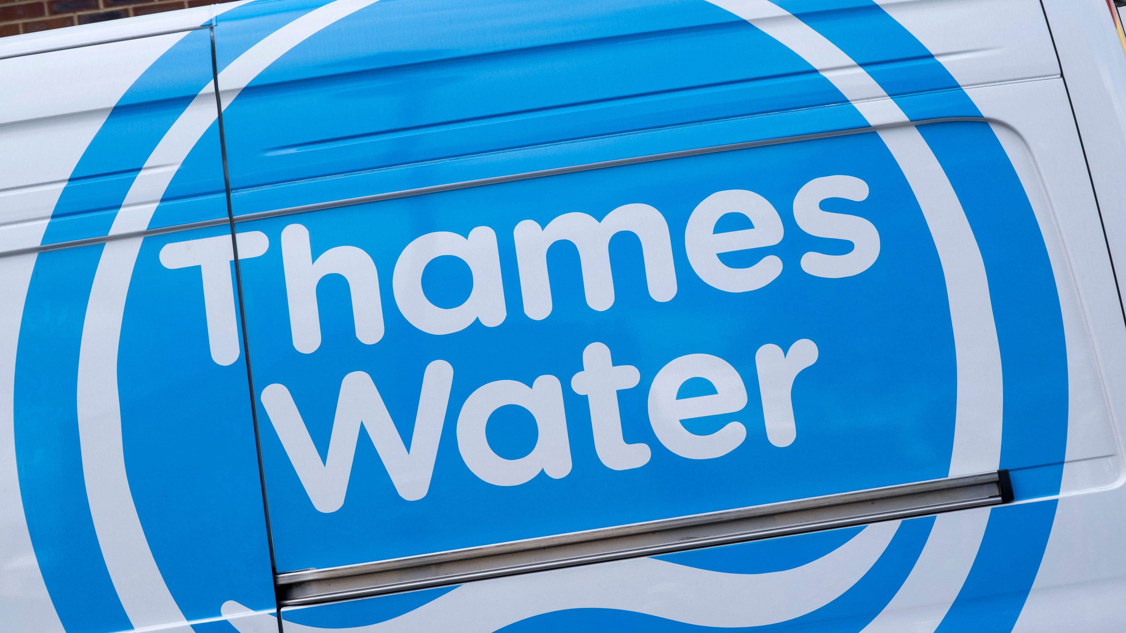 Blue and white Thames water logo on a van. It is close up. The logo is a blue circle with Thames Water written in white writing. There is a white wave below the writing.
