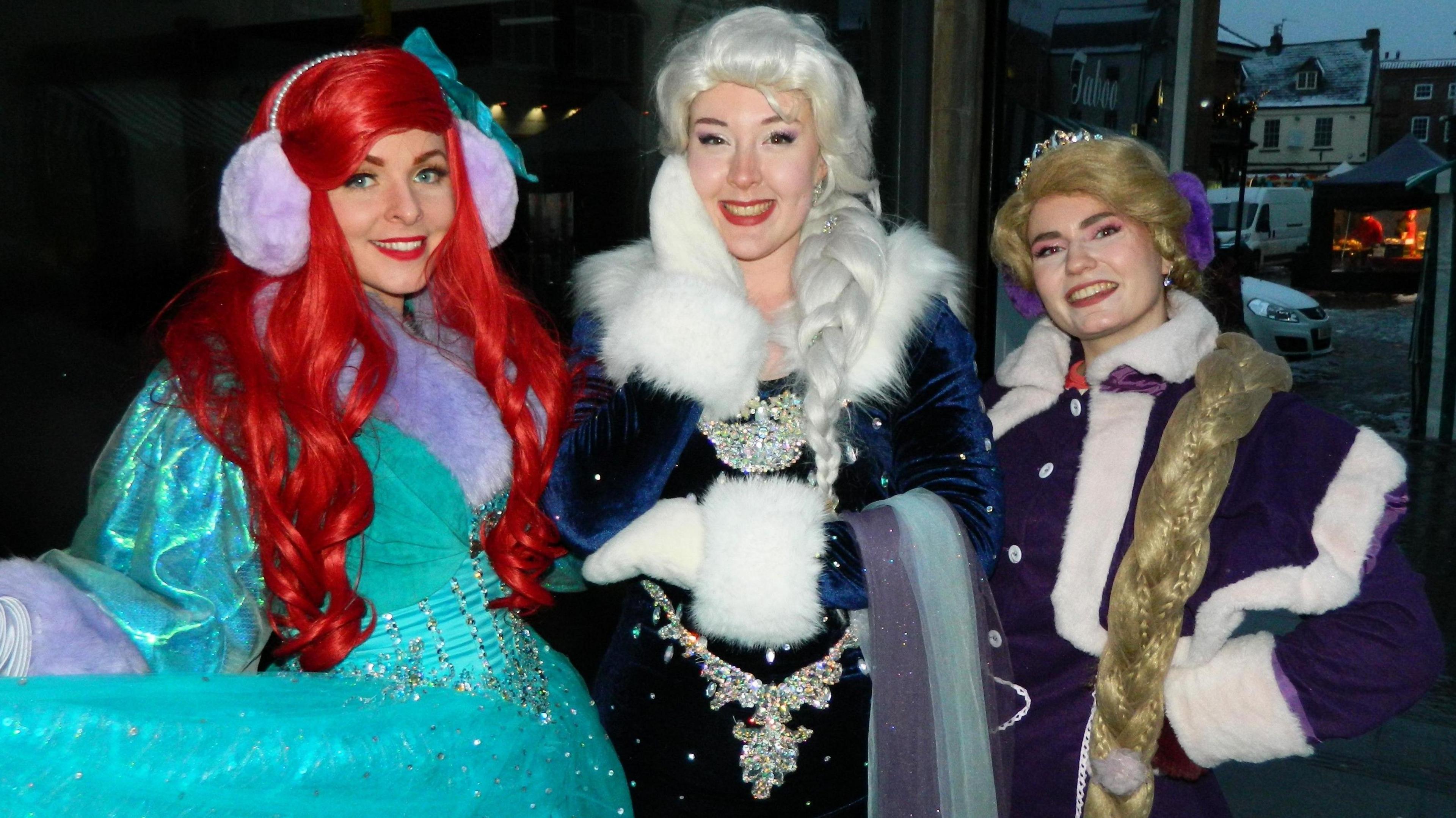 Three women dressed as Disney characters Ariel, Else and Anna, complete with fancy wintery costumes and big wigs. 