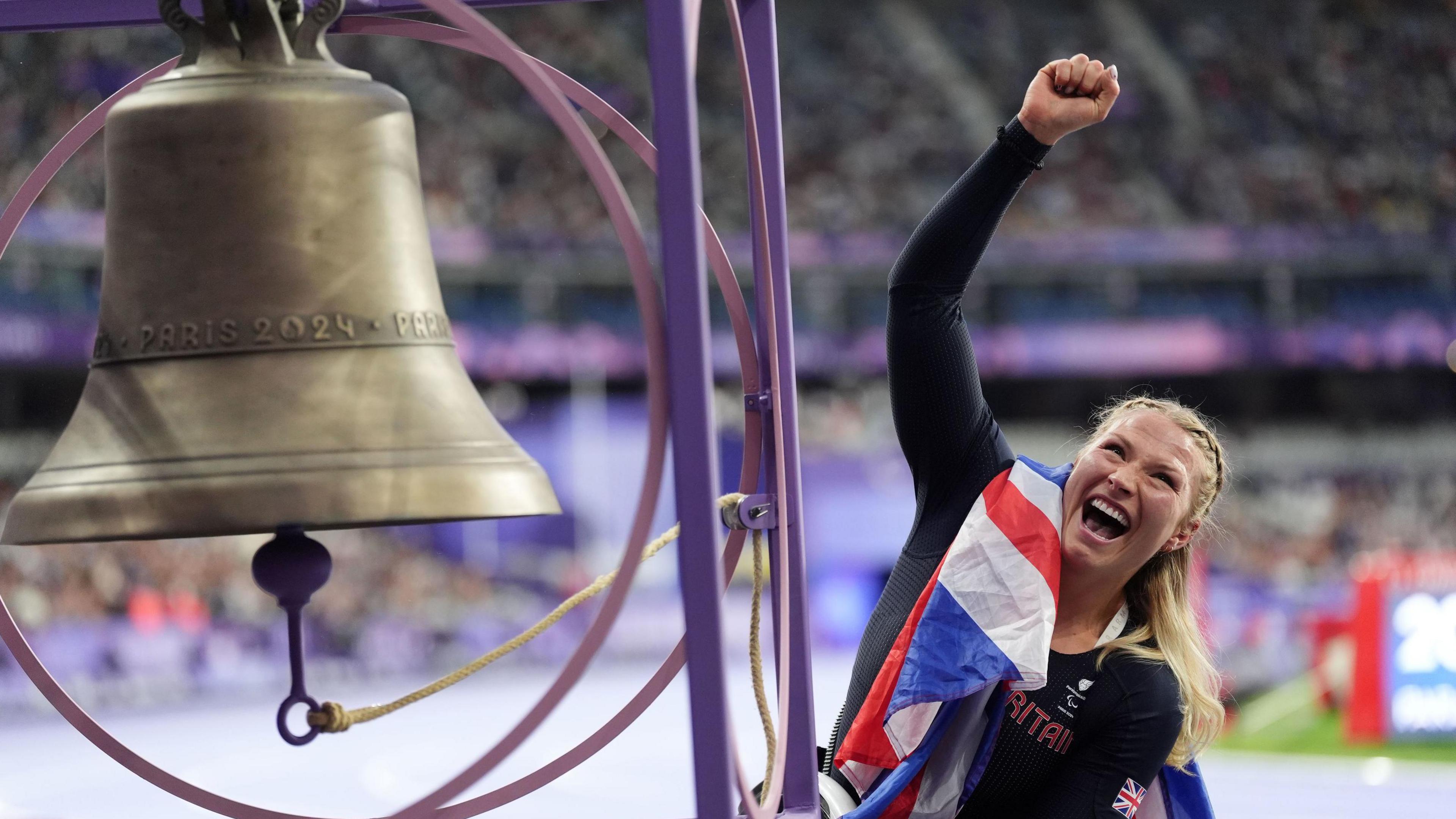 Sammi Kinghorn celebrates and rings the victory bell after winning the T53 100m at the Paris Paralympics