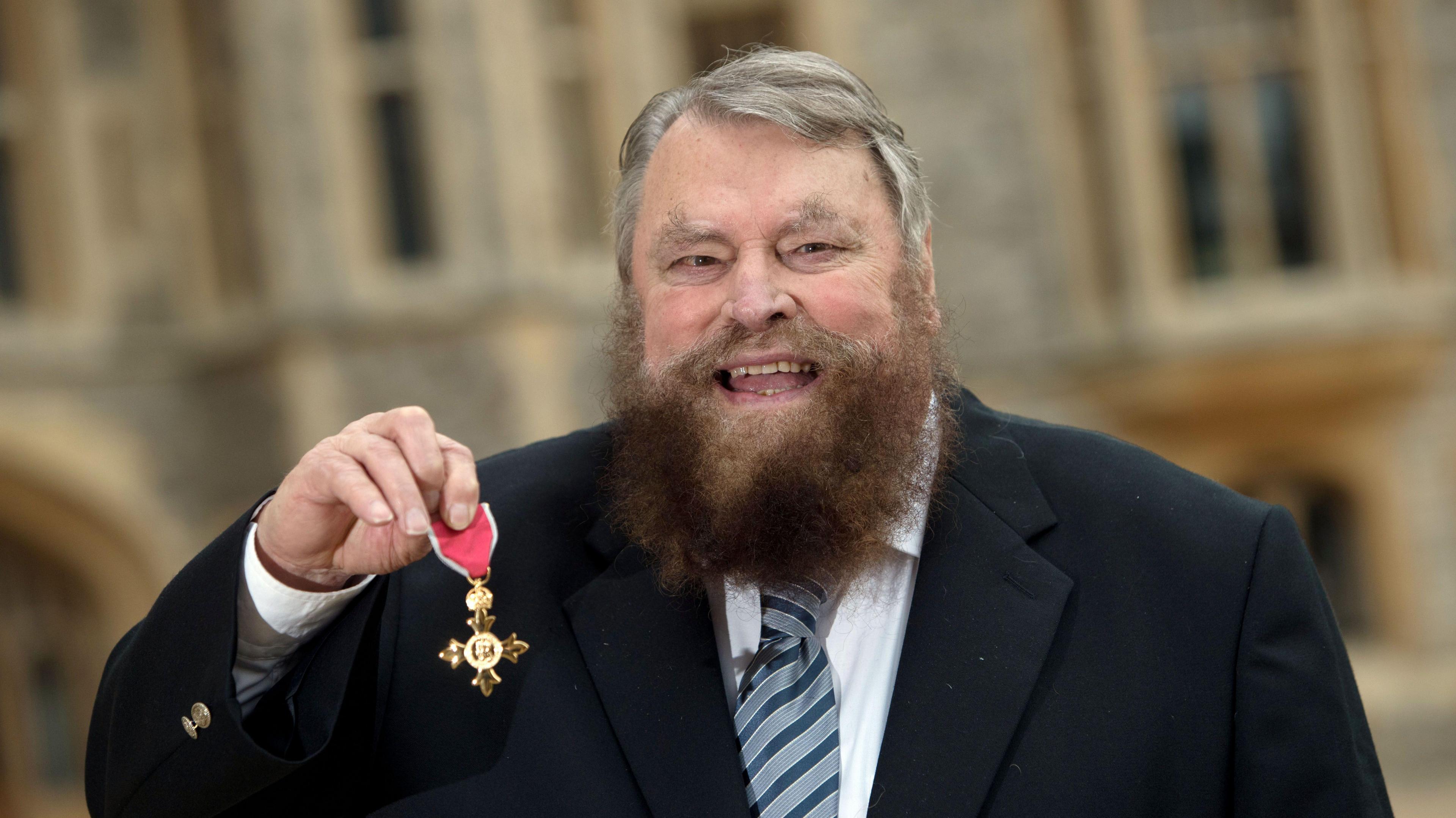 Brian Blessed holding up his OBE after his investiture ceremony at Windsor Castle