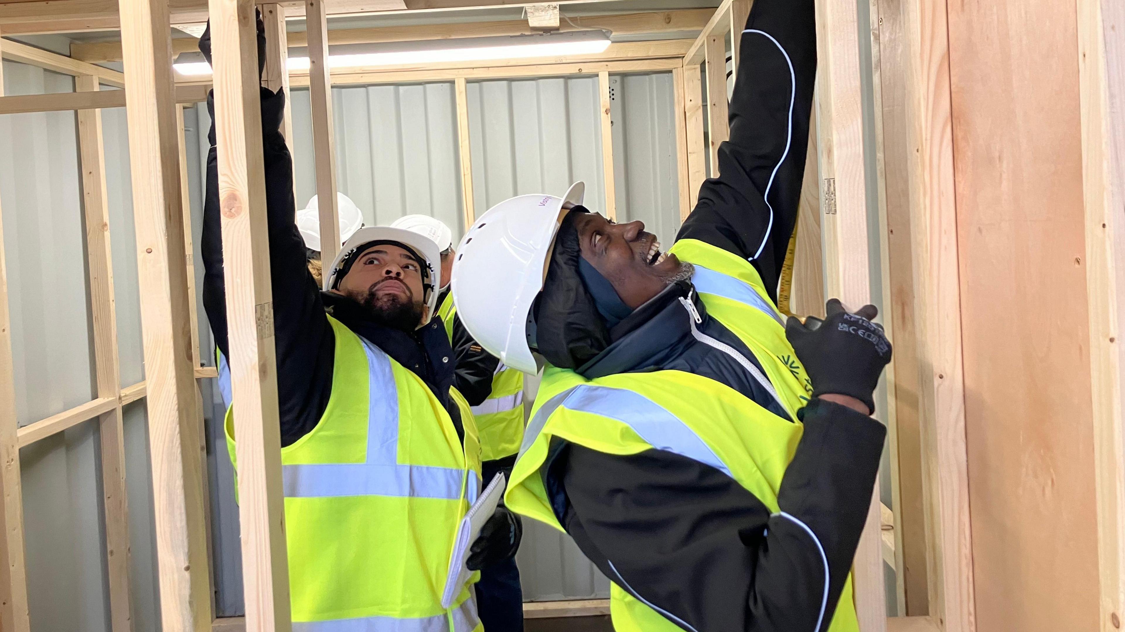 Two men in hi-vis constructing timber frames