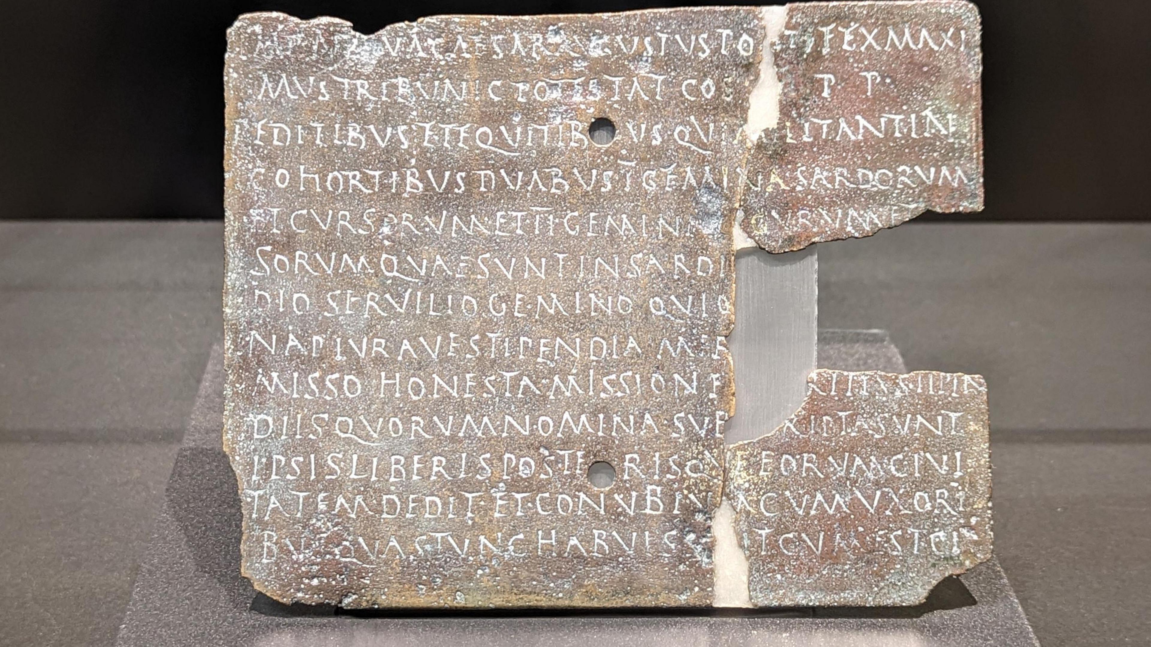 A square stone coloured plaque with a big chunk on its right hand side missing