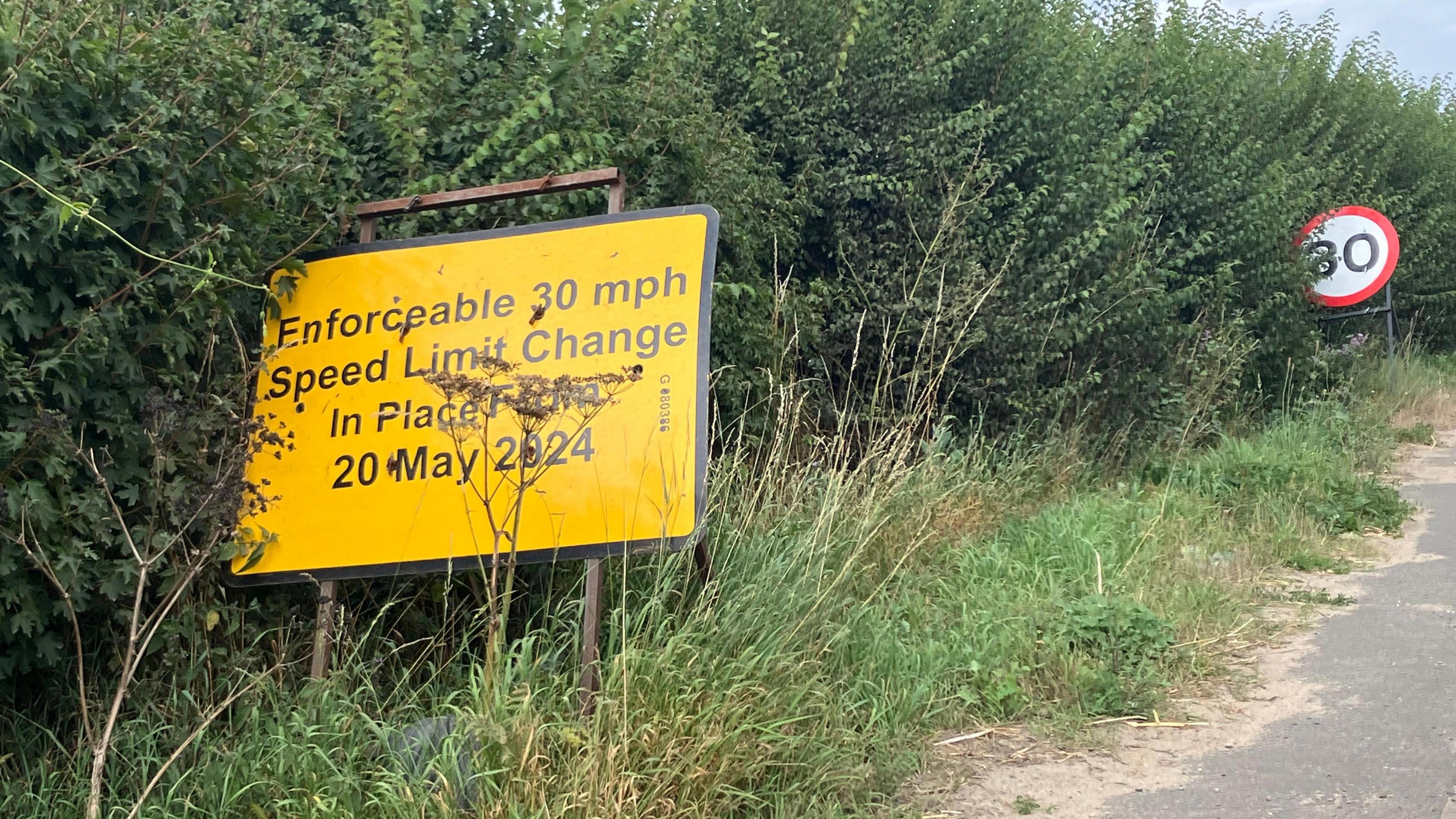 A yellow road sign alerts drivers to "Enforceable 30mph speed limit change in place"