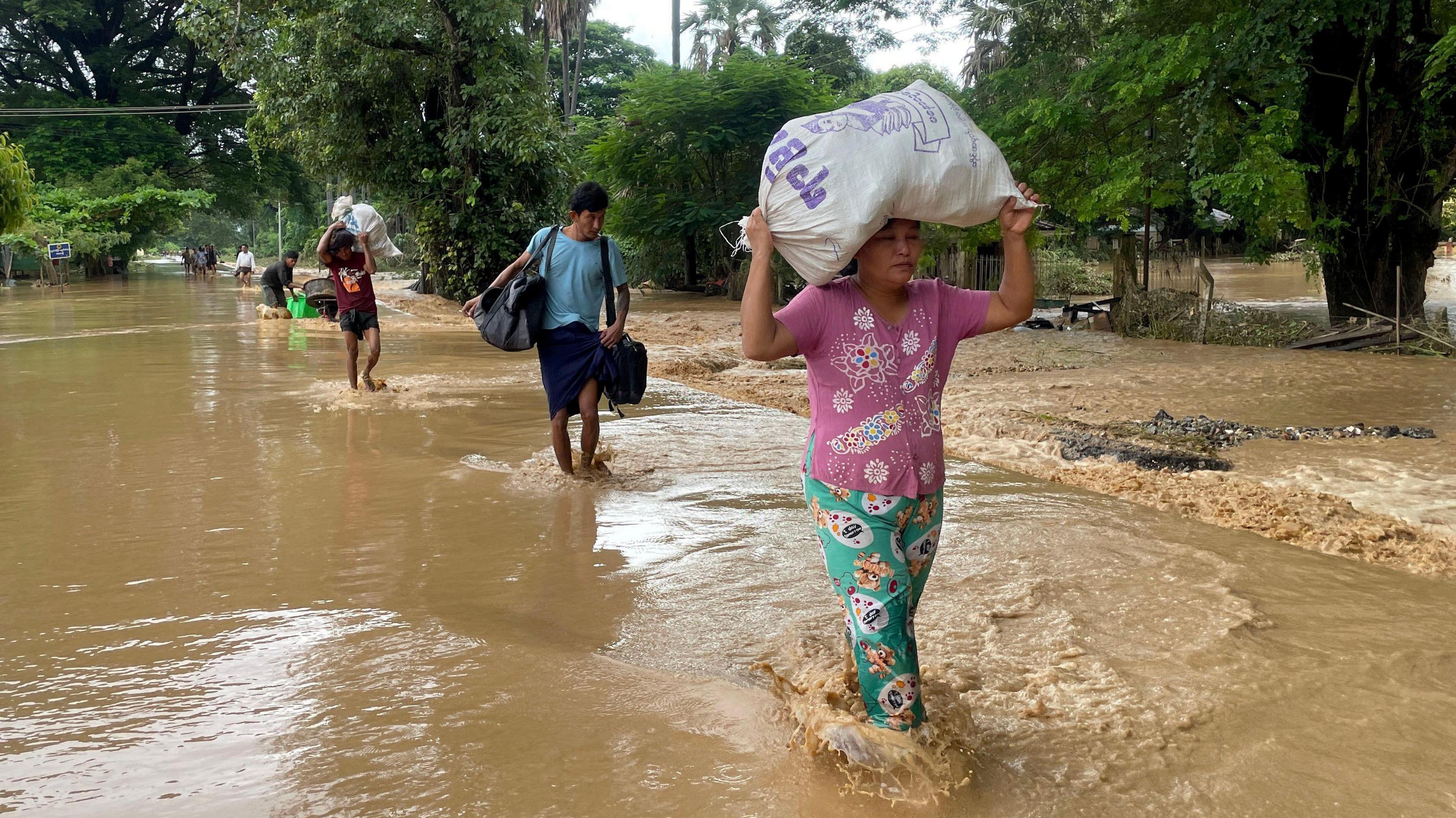 People carry their belonging as they wade through flood waters in Pyinmana, Naypyidaw, Myanmar, on 13 September 2024.